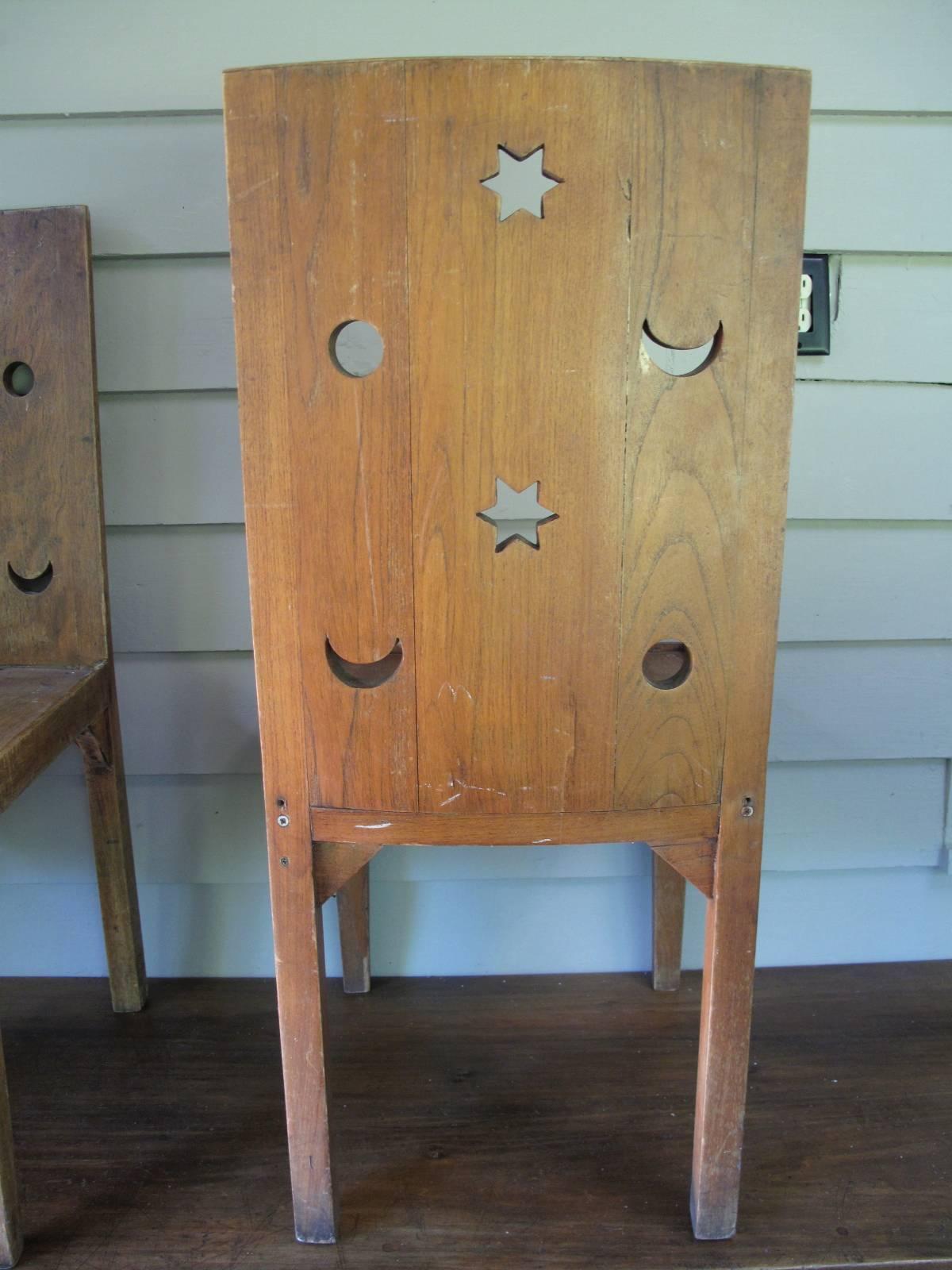 Set of four handmade oak chairs, each having sun, moon, and stars shapes cut from back panels. Seats have a shallow recess intended to hold a cushion as shown. No apparent signature or makers mark.