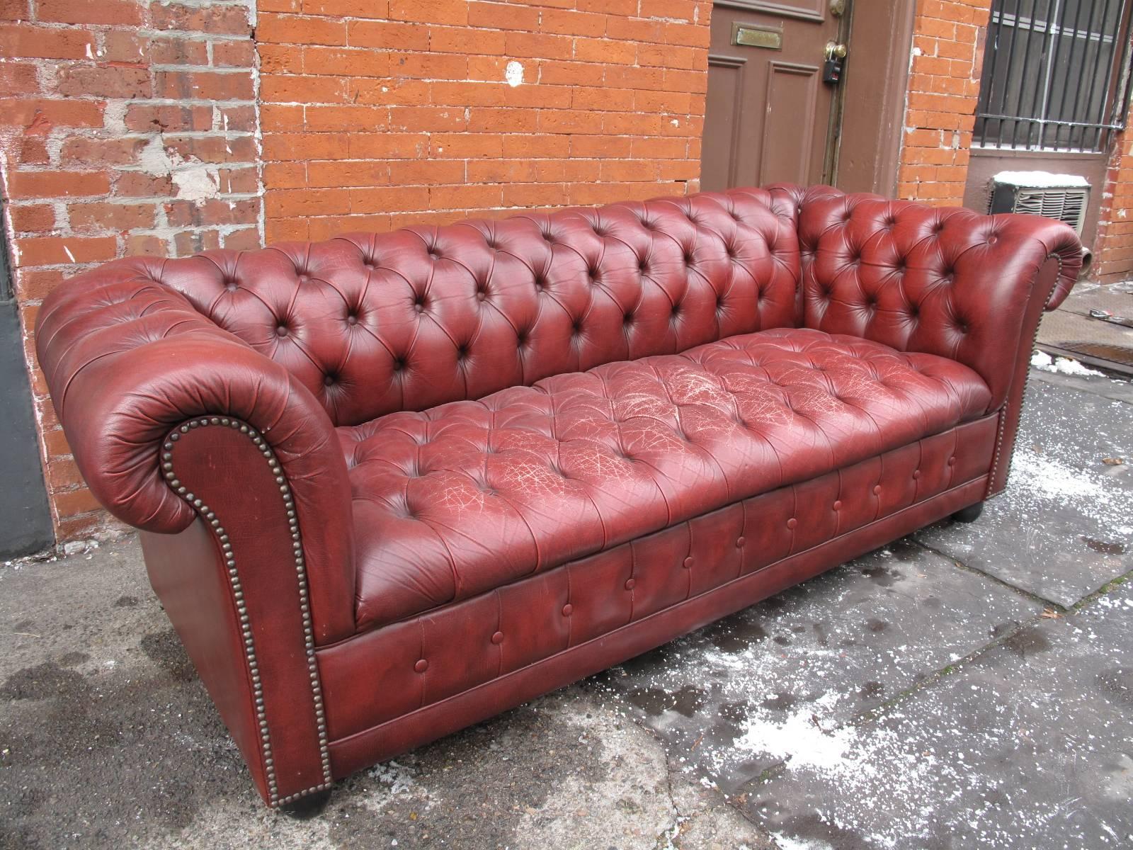 Tufted oxblood leather sofa. Made in England in the mid-later 20th century. Ebonized ball feet.