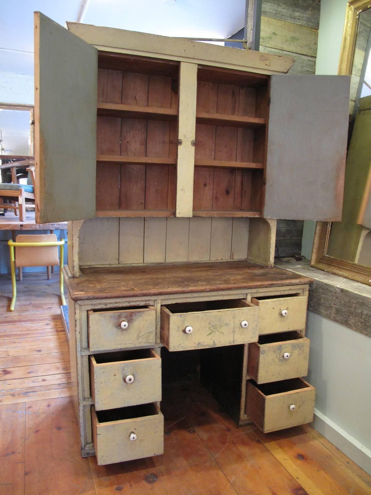 Two part cupboard in original paint having seven drawers at base. Small white porcelain knobs. Primitive hand-hammered nail construction.