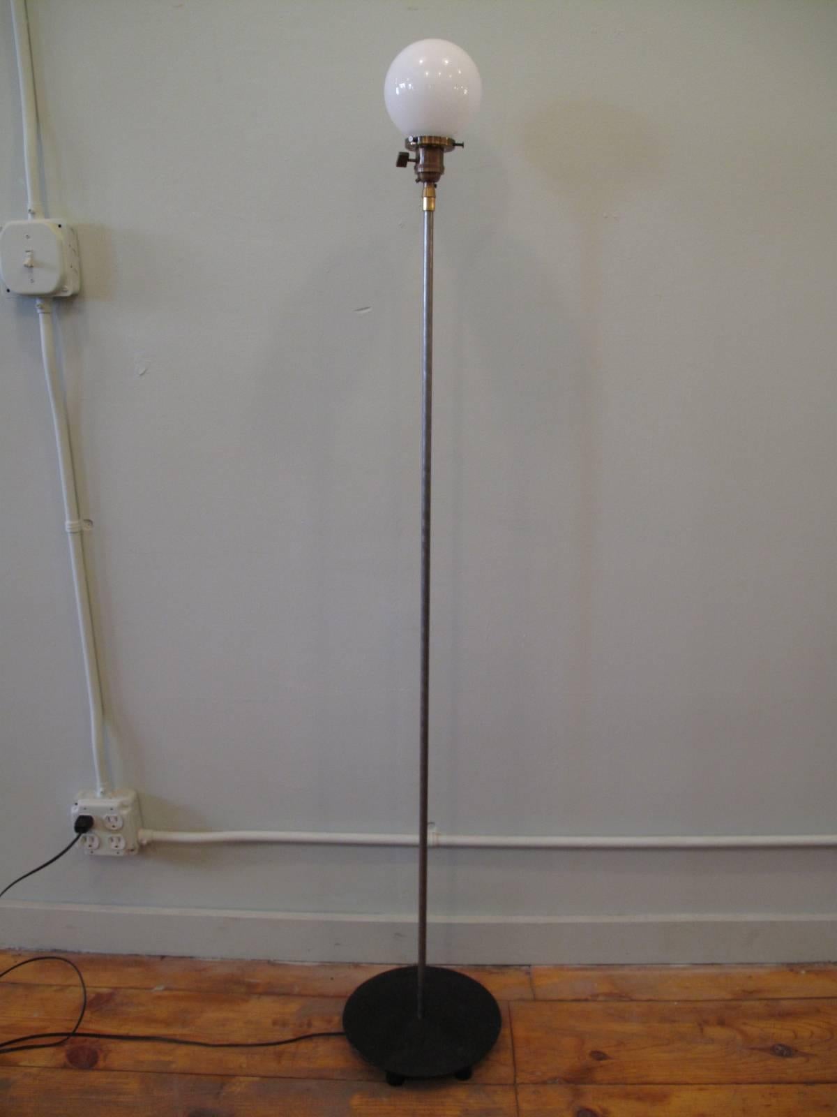 Single light floor lamp on weighted iron base. Milk glass globe sits in antiqued brass fitter. Raw steel body. 

Globe measures 5" in diameter

Please note: This lamp is currently in working condition. However, we recommend that all