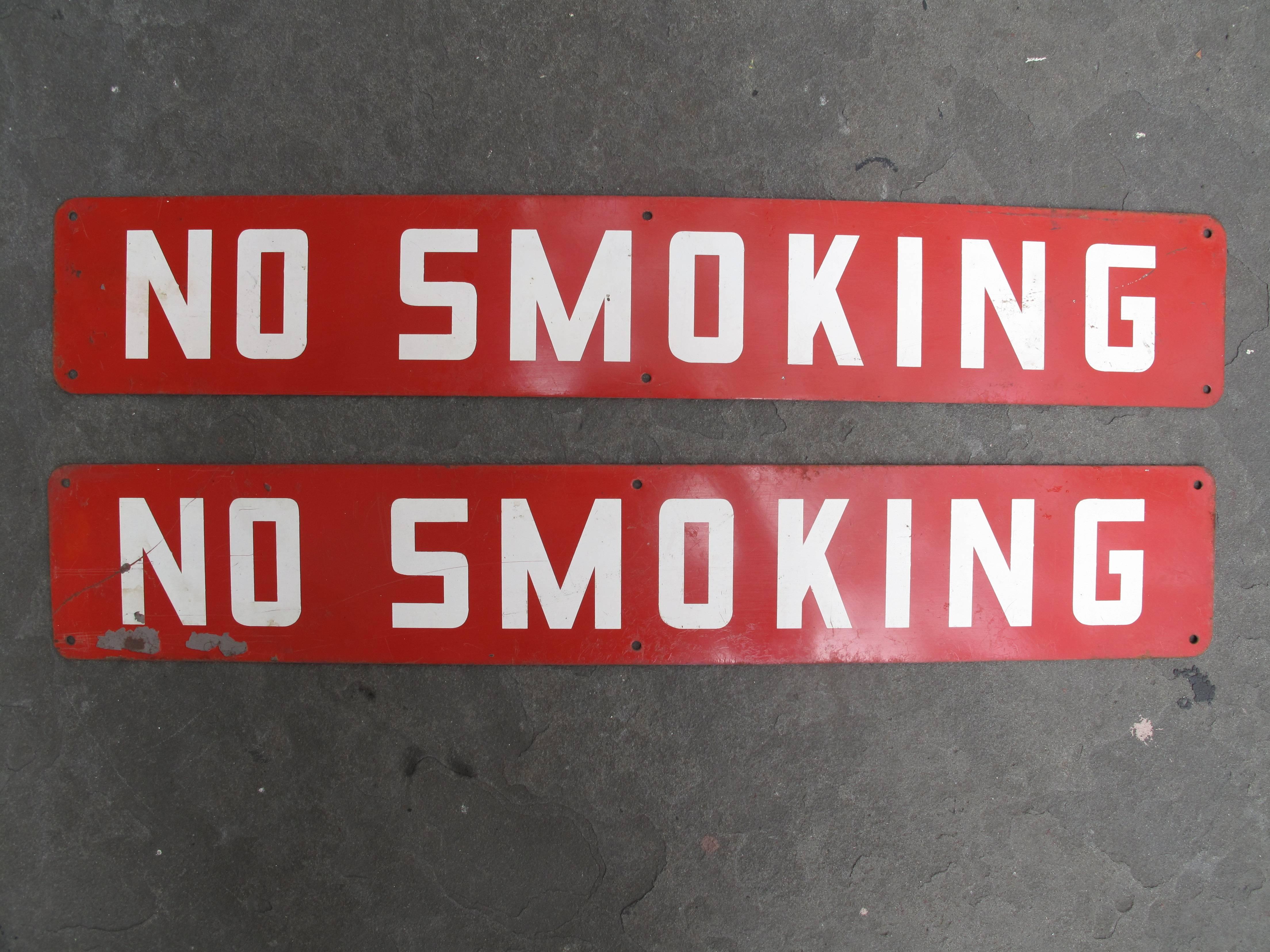Two matched sheet metal signs with red and white enamel lettering reading NO SMOKING. Each having six small holes for screws. Backs are blank.
