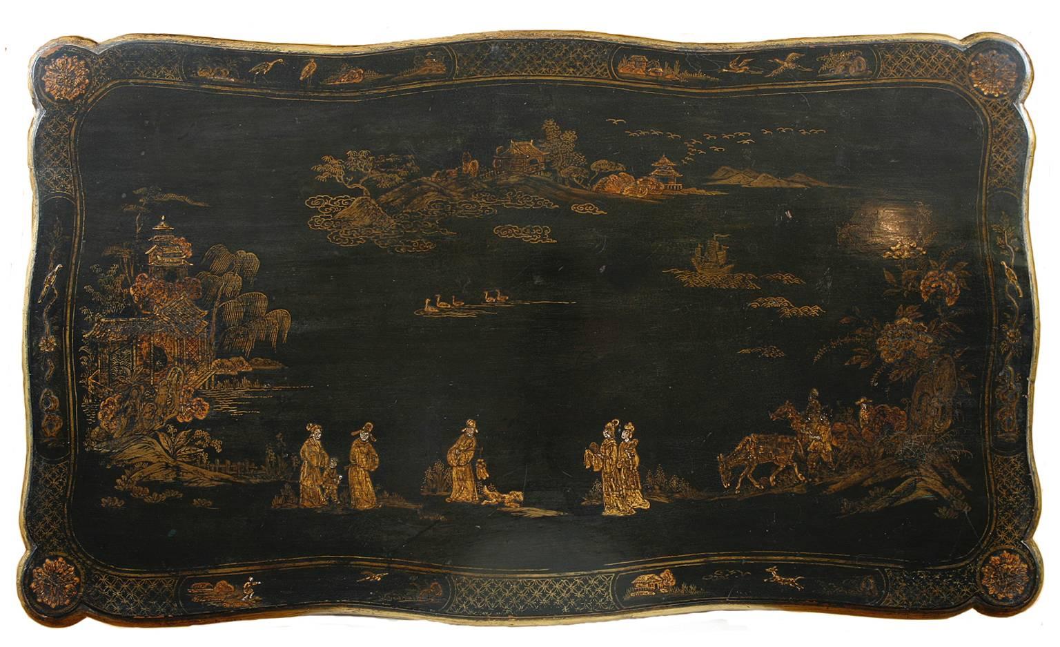 A very lovely chinoiserie table in black lacquer with decorations in gold paint of scenes from Chinese village life that include: Men astride horses holding nets with dogs afoot, women strolling along a path with pagodas and houses in the distance