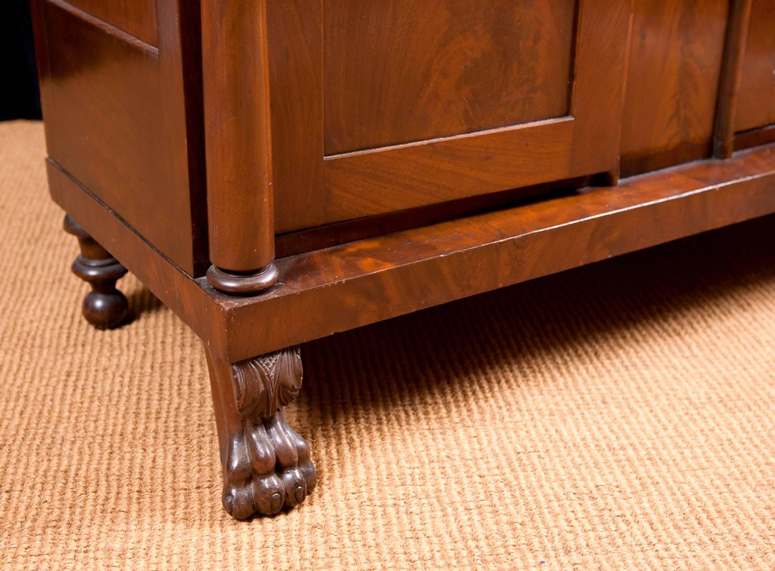 A fine petite American Empire sideboard in mahogany and bookmatched figured mahogany. Features rectangular top over two drawers above base cabinet with two doors flanked by turned ionic columns, resting on carved lion's paw feet and turned back