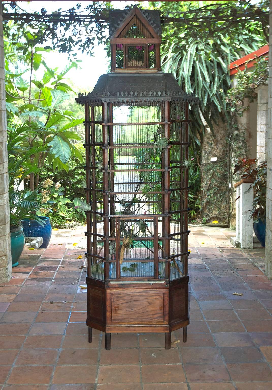 An exquisite and functional French aviary intended for use as a breeding cage, with the cupola housing a removable smaller cage for the introduction of new birds. The aviary has a teakwood frame with steel bars and a galvanized metal roof, and may