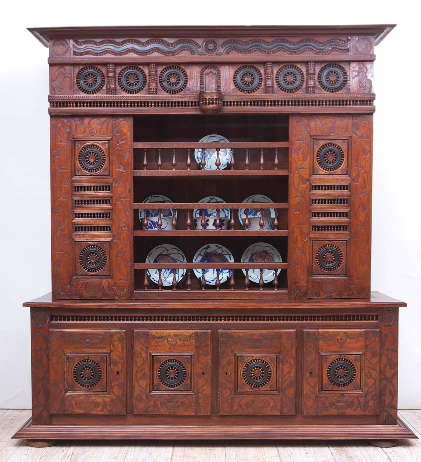 A strikingly handsome and very unusual cupboard in Jarrah wood and polychrome wood with decorative carvings depicting birds, pinwheels, foliage and flowers. Offers several open shelves with galleries with turned finials that serve to hold dishes,