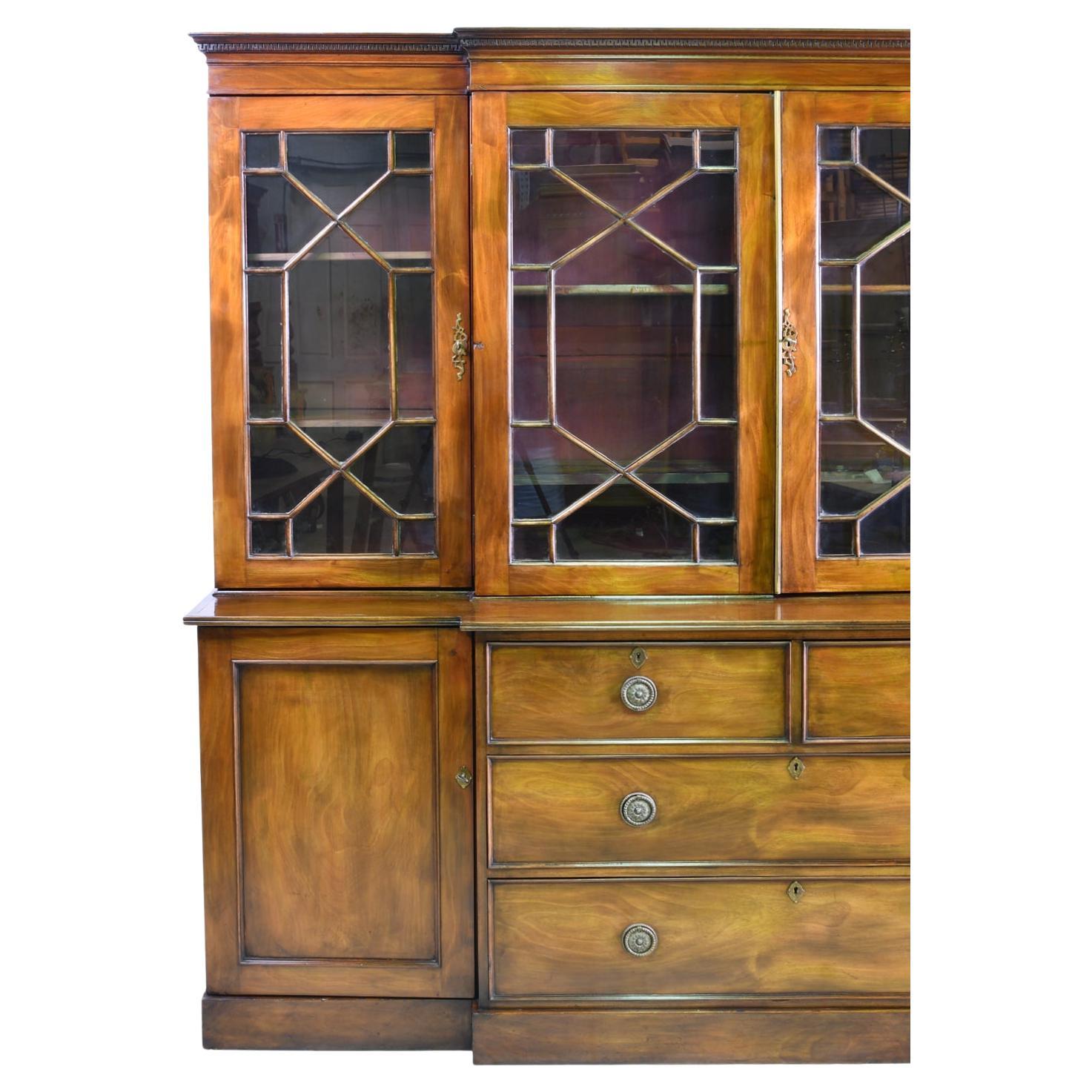 19th century English breakfront bookcase in the Georgian style dates from circa 1870. Glass doors have actual muttons with individual glass panes. Bottom has a flight of drawers in the center with 2 small drawers over 2 long drawers. Drawer pulls