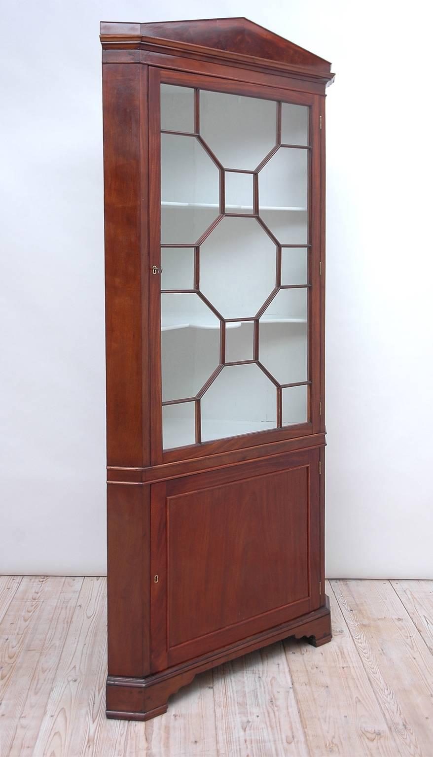 An English Regency corner cupboard in mahogany with pediment top, glazed and mullioned upper cabinet over paneled cabinet, and resting on bracket feet. England, circa 1820.
Measures: 33