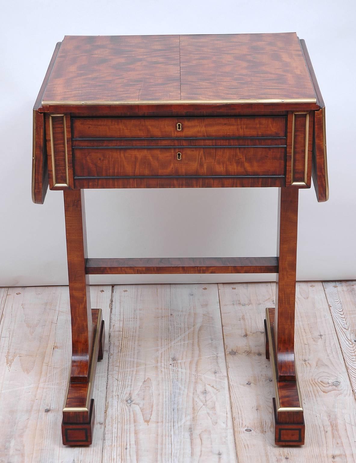 A fine English Regency work or side table on trestle base with drop leaves in beautiful plum mahogany with brass banding on edge of table and ebonized banding around drawers and block feet. Back and front of table are identical with front offering