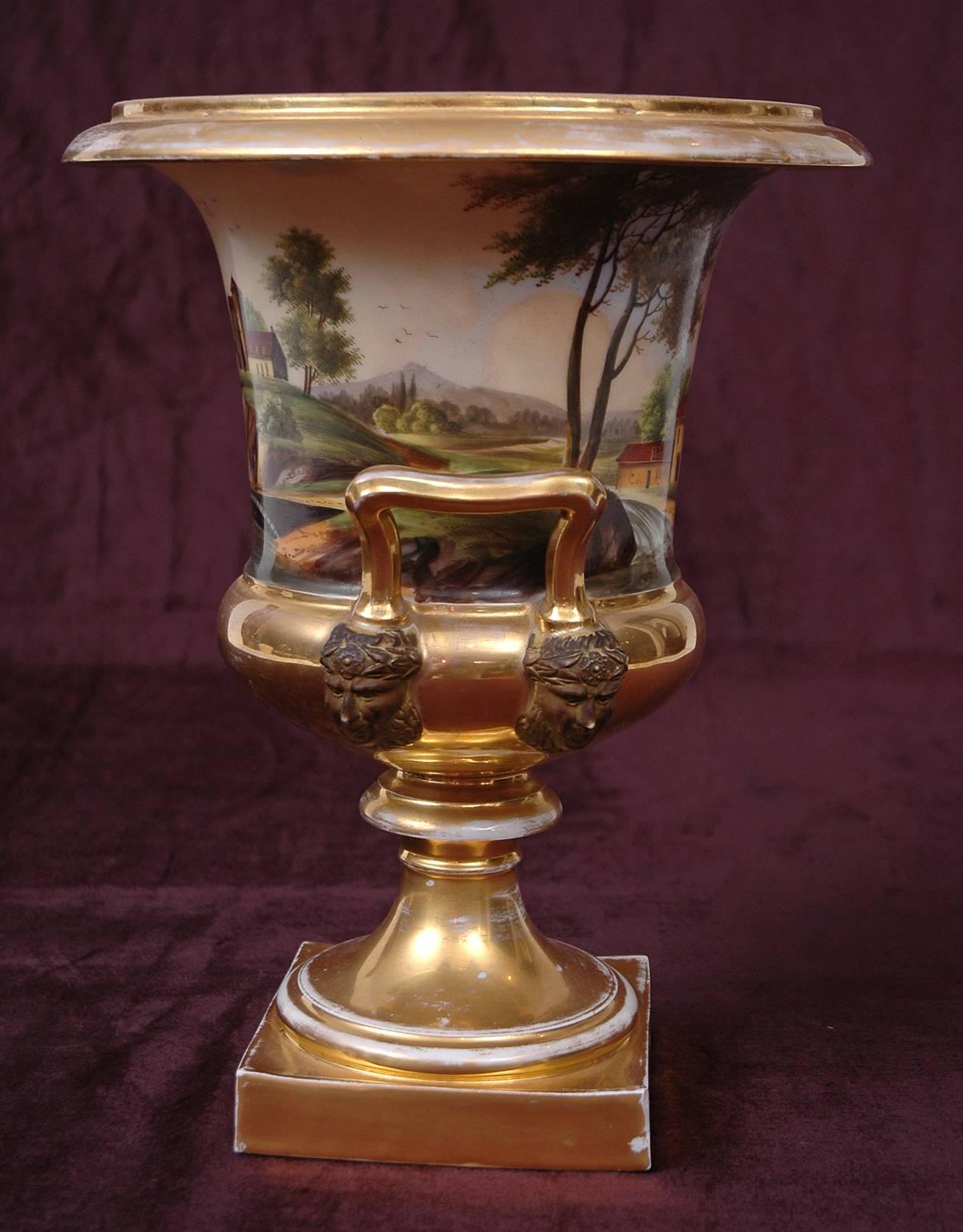A large campagna urn with beautifully painted country scenes (possibly of chateaux in Arces, France). Sculpted figureheads adorn inverted handles, with gilding on rim, handles, pedestal and square base, France, circa 1820.

Measures: 10.25