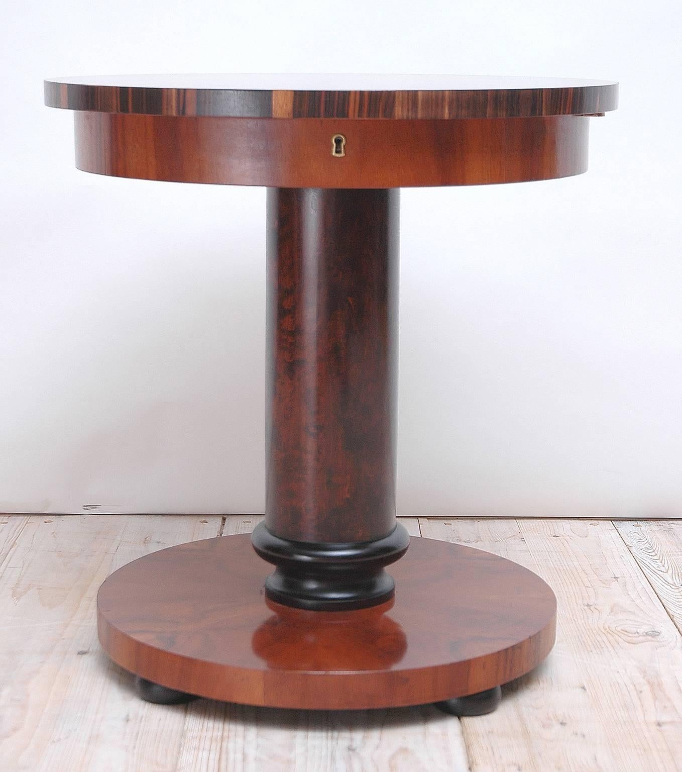 A round Art Deco end table in Massacre ebony and mahogany with cylindrical pedestal column resting on round base. Top swivels open to reveal interior compartments. Originally sold through, and possibly commissioned by, the Swedish department store