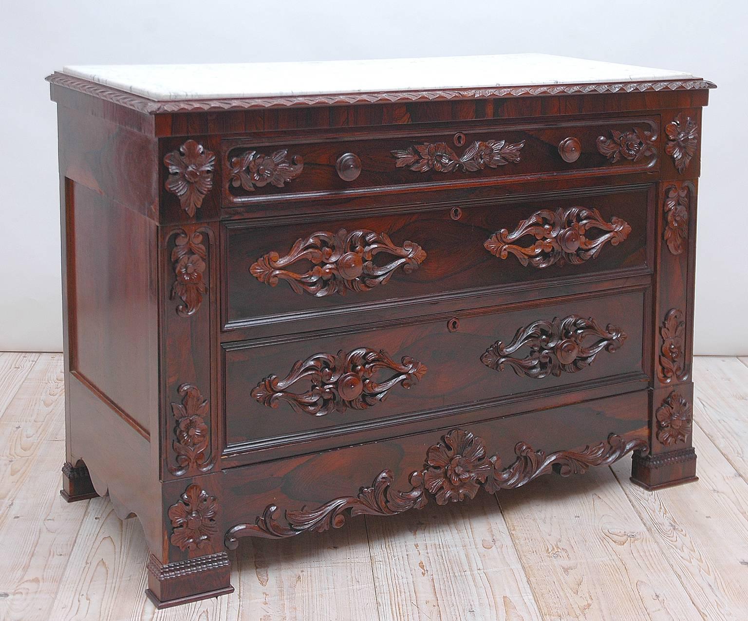 A beautifully-carved & highly decorated Victorian chest of drawers in prized rosewood with original statuary marble. Features original and complete carved rosewood appliqués and knobs, with gadrooned edge and inset marble top. American, circa