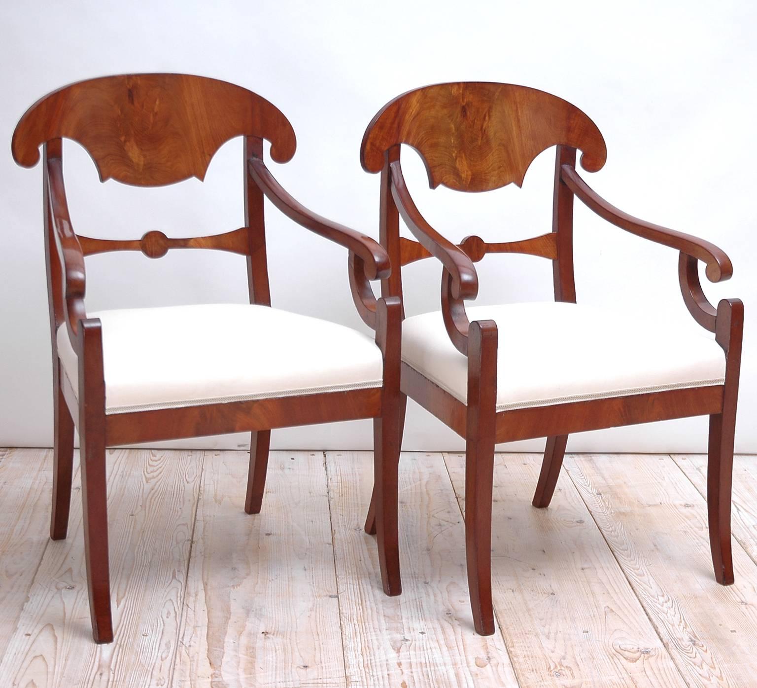 A pair of Karl Johan arm chairs in figured mahogany with shovel-shaped backrest, recessed volute arms, upholstered seat and saber legs. In the more subdued Swedish interpretation of the French Empire style, they offer an understated elegant, almost