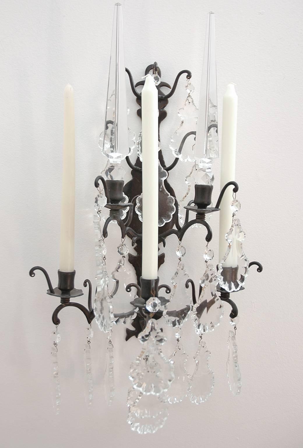 Set of four bras de lumiere wrought-iron sconces with Czechoslovakia cut-glass/crystal prisms, pendants and obelisks. Open cage form with six arms: Two for obelisks and three for candles.

Provenance: Designer Rybar Valarian with his partner