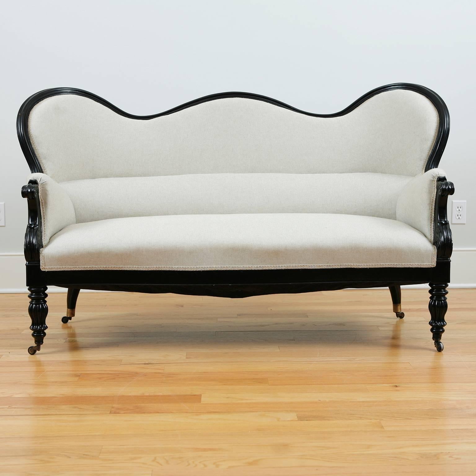 Period French Napoleon III sofa in ebonized wood, with triple hump-camel back and turned and fluted front legs resting on casters, with upholstered seat and back, France, circa 1870. Original four chairs trhat came with suite are also available on