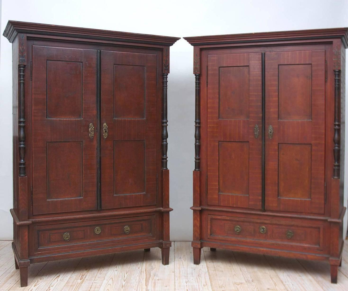From the Austro-Hungarian Empire, a nearly identical pair of armoires with ebonized columns and astragal, and the original tooled and grained finish. Offers divided storage with adjustable shelving, primitive hanging rod in one and a small original