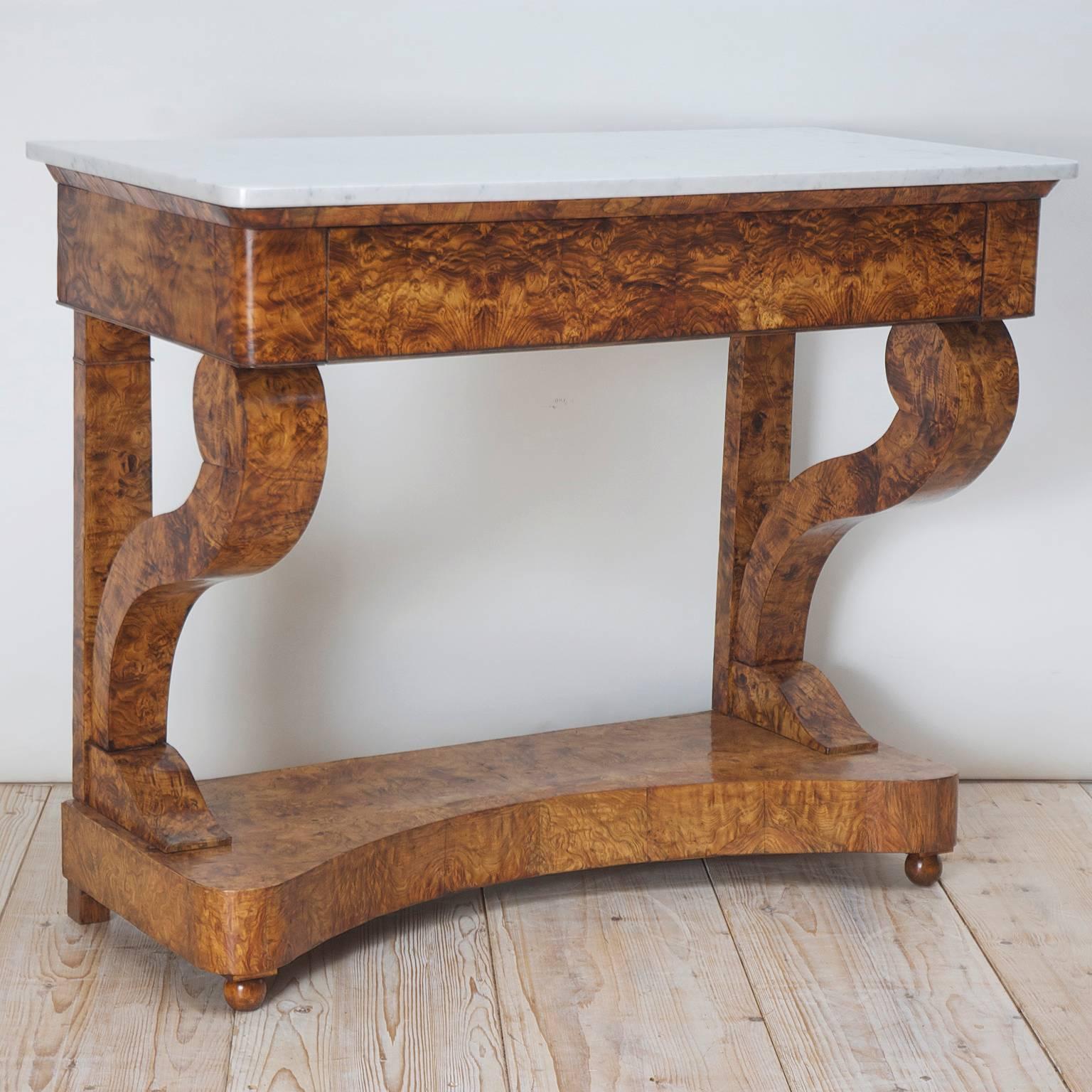 An Empire or Biedermeier Console in burl olive-ash with white Carrara marble top. Offers a drawer with two volute columns that rest over a concave base and terminate in small turned ball feet. The grain of the wood is exceptionally beautiful!