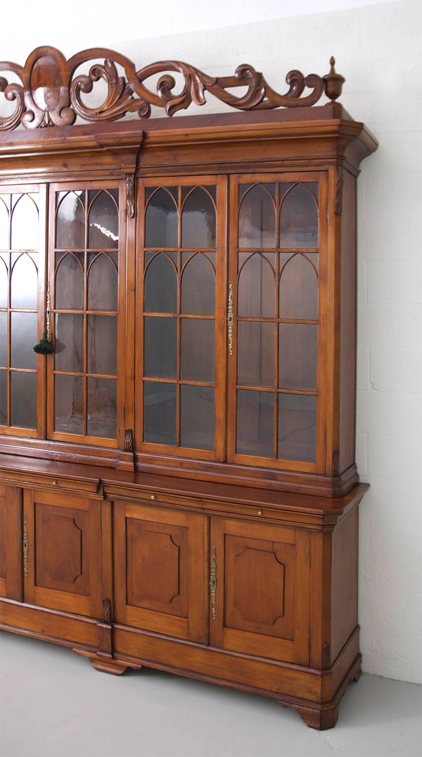 A monumental Louis Philippe breakfront bookcase, bibliotheque, measuring over 10 1/2 feet in length, in sycamore with original glass panes featuring arched mullions on upper cabinet, raised wooden panels on lower cabinet, and six exterior drawers in