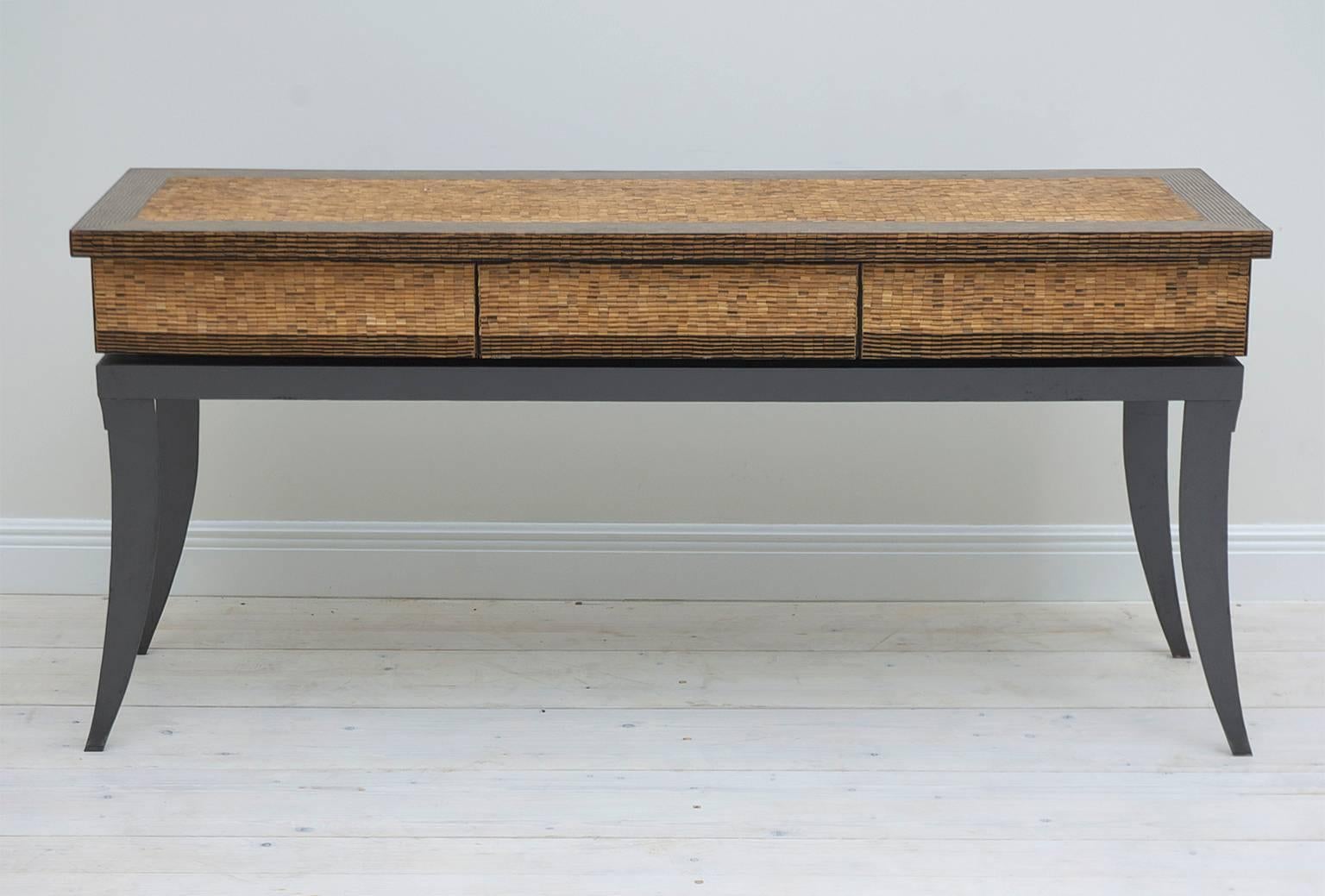 A very beautiful narrow table with sleek lines, featuring a finely inlaid top of split bamboo and palmwood, resting on anodized steel base with saber legs, and offering three drawers. Thailand.
A handsome sideboard, entrance or sofa