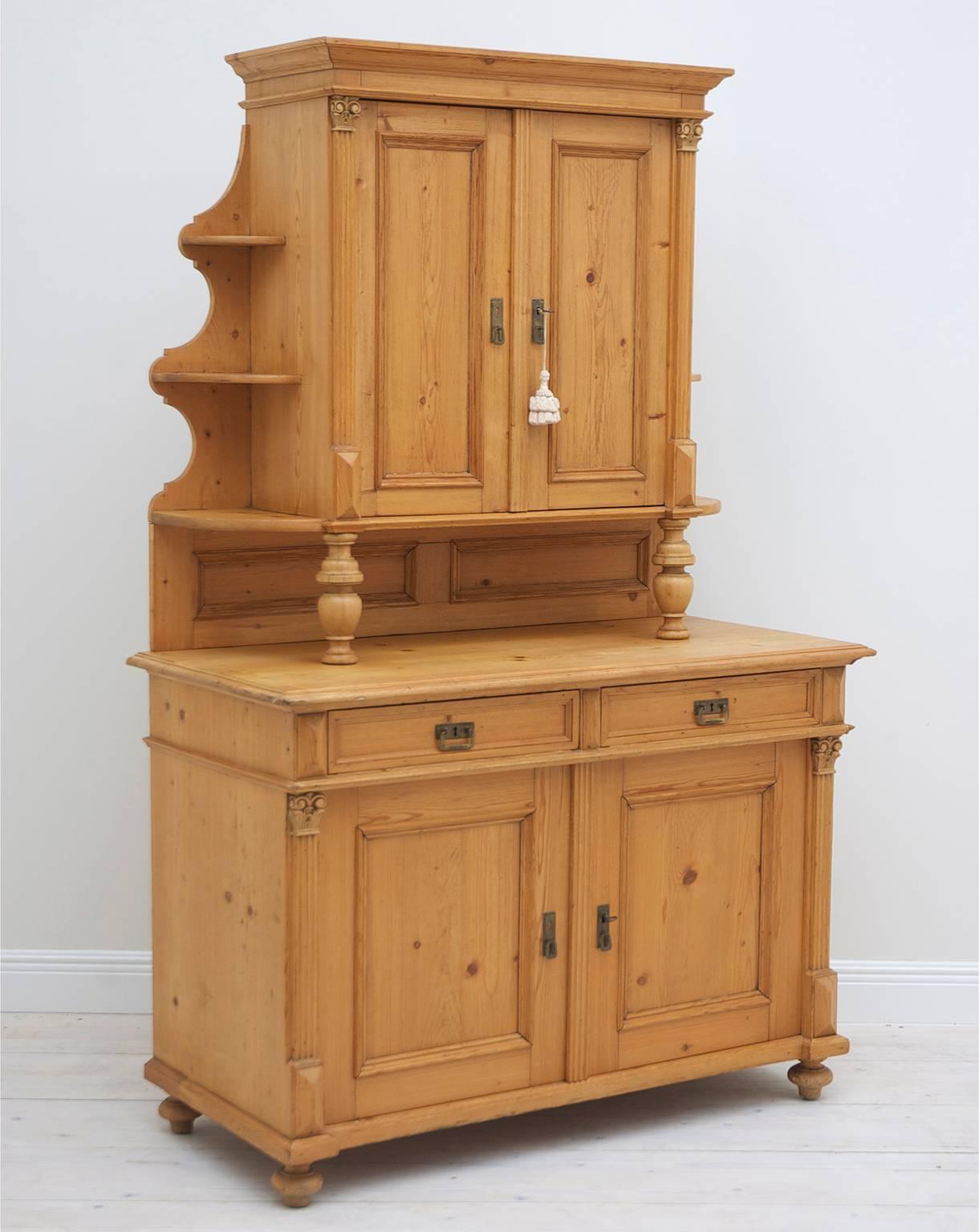A charming cupboard in pine from the rise of the German Republic, circa 1880-1890. Upper cabinet is separated from the lower cabinet by a paneled back splash and turned front pillars. Both sets of doors are flanked by fluted pilasters topped with