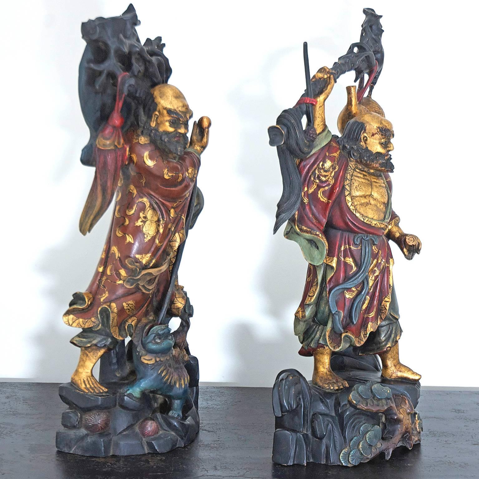 A pair of Chinese sculptures in the Ming style, expertly carved in wood with a polychrome finish, depicting bearded male figures in flowing robes holding branches over their shoulders on a rocky base. China, early 1900’s, or possibly late