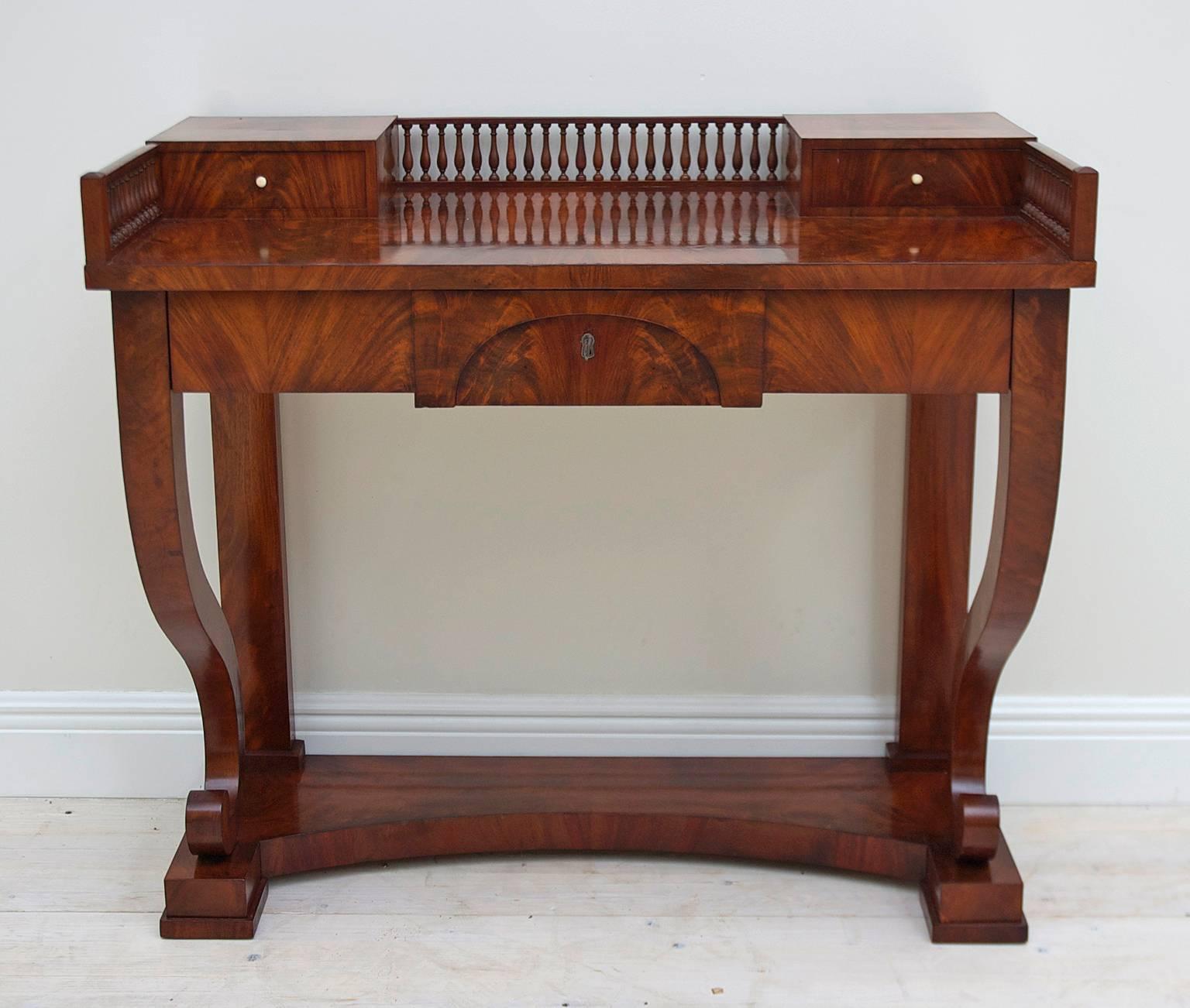 A very lovely Swedish Empire Karl Johan writing desk or dressing table in West Indies mahogany with two small drawers flanking a center gallery and one long storage drawer on apron. Two volutes act as front supports and lend a graceful and light