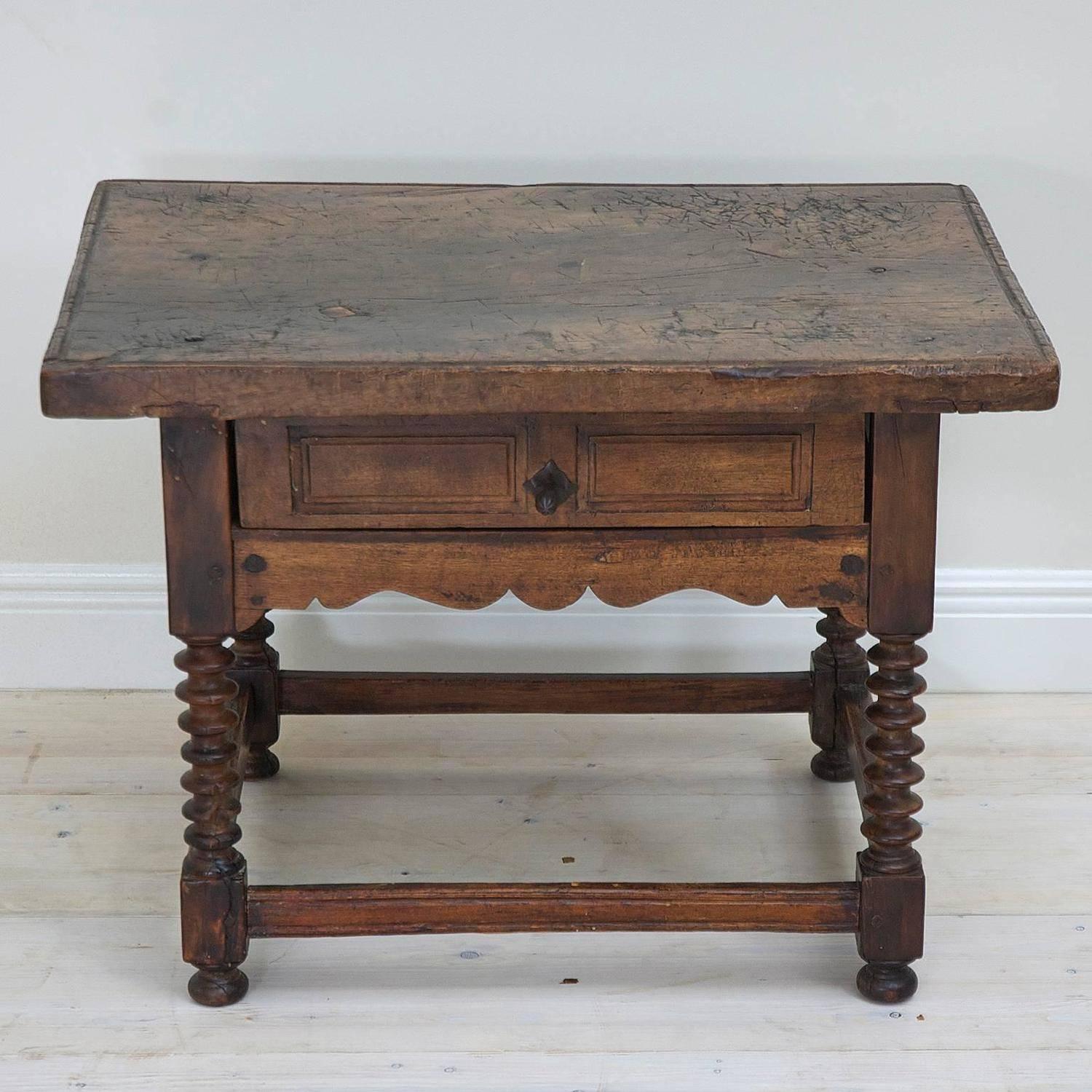 A charming Spanish 18th century Baroque table in walnut that historically was used by a cobbler and features a weathered top that attests to the hammering work involved in the process of making and repairing shoes. The base offers a storage drawer