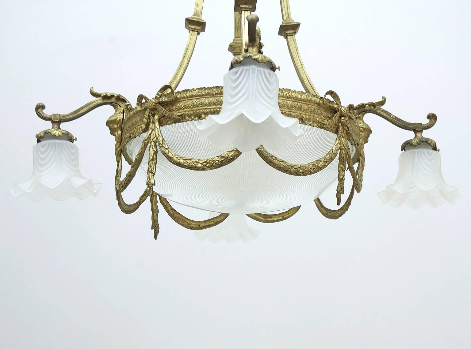 A lovely French Belle Epouque chandelier in bronze doré with eight lights featuring Louis XVI style swags and bows with fluted and flounced glass globes.

Measures: Drop: 36" x Diameter: 32".