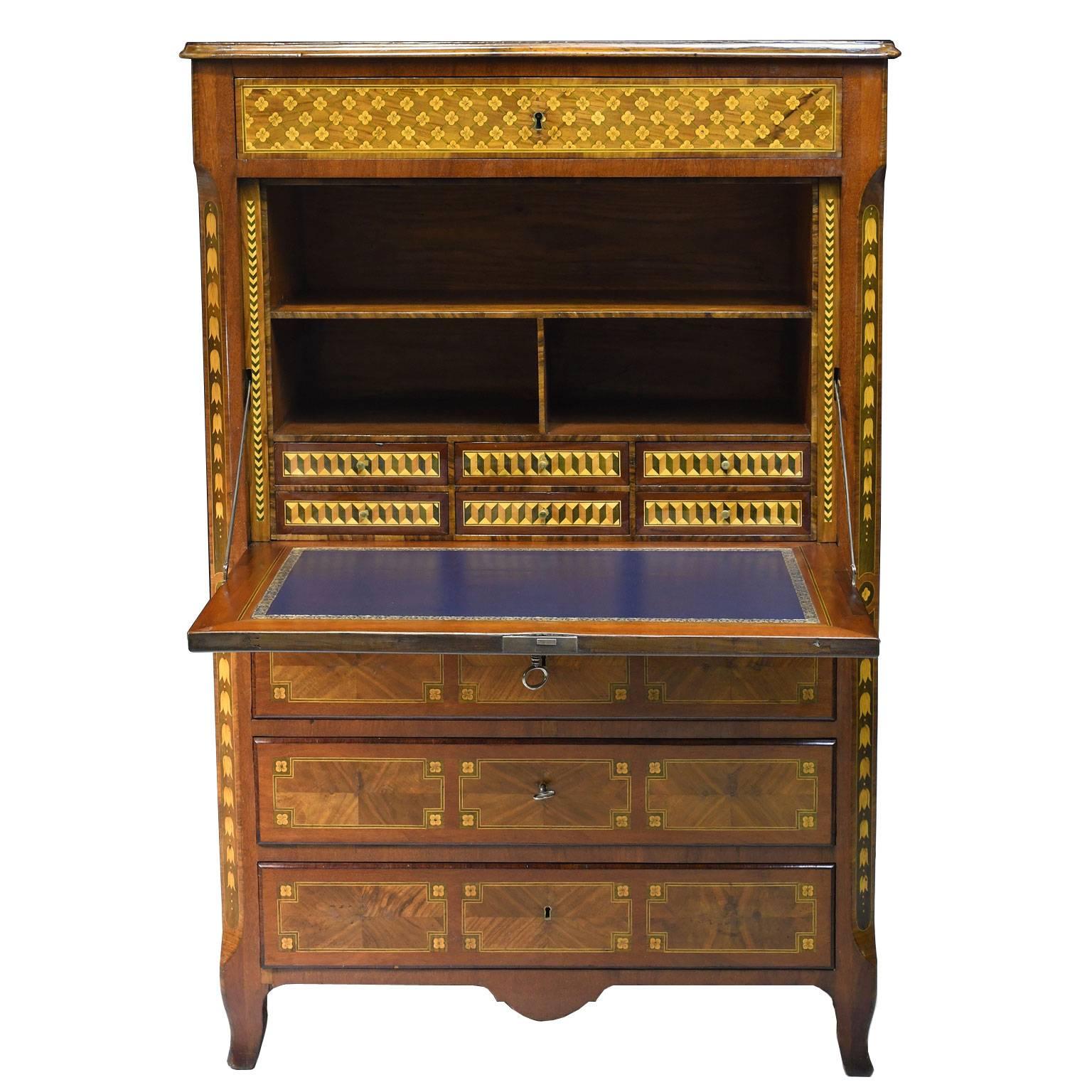 This understated but elegant bureau cabinet is composed of three sections decorated with colorful and contrasting marquetry throughout, depicting ornamental motifs using lemonwood and eucalyptus over mahogany. 
The upper section offers a drawer