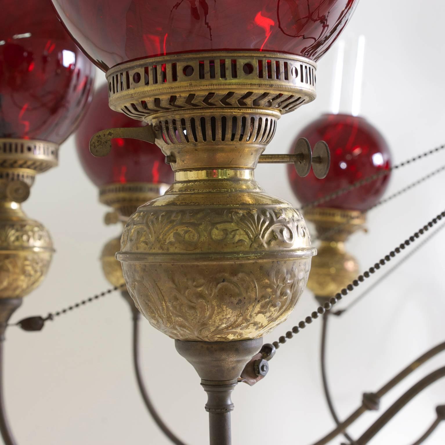 A ten-light chandelier in hand-hammered brass with glass chimneys and cranberry glass globes, England, circa 1860-1880.
Chandelier has been electrified. 
Drop is 25" without the chimneys x 58" in diameter.

Manufacturer's name is