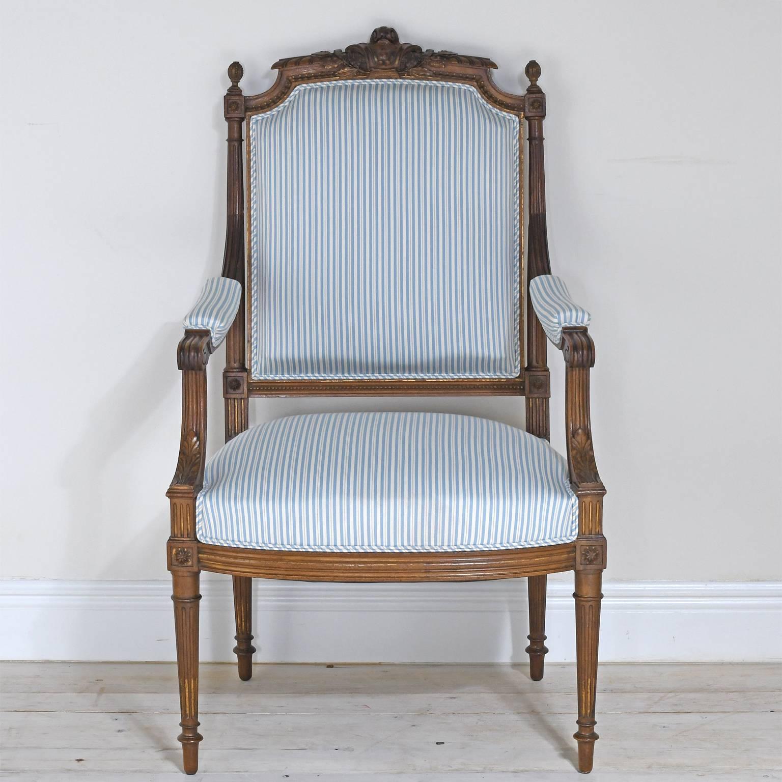 A very lovely pair of Louis XVI style French fauteuils with walnut frames offering well-articulated carvings which include a carved back crest with a cartouche flanked by oak leaves, scepter finials, boss rosettes, acanthus leaves on arm supports,