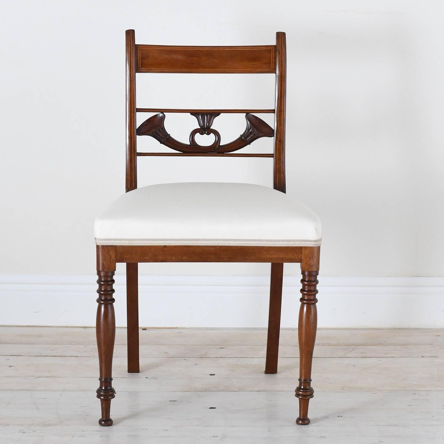 A fine set of four English Regency dining chairs in mahogany with carved bugles resting on back chair rail below the top slat which is line inlaid, with turned front legs and saber rear legs, and upholstered seat, England, circa 1830.

Measures: 19