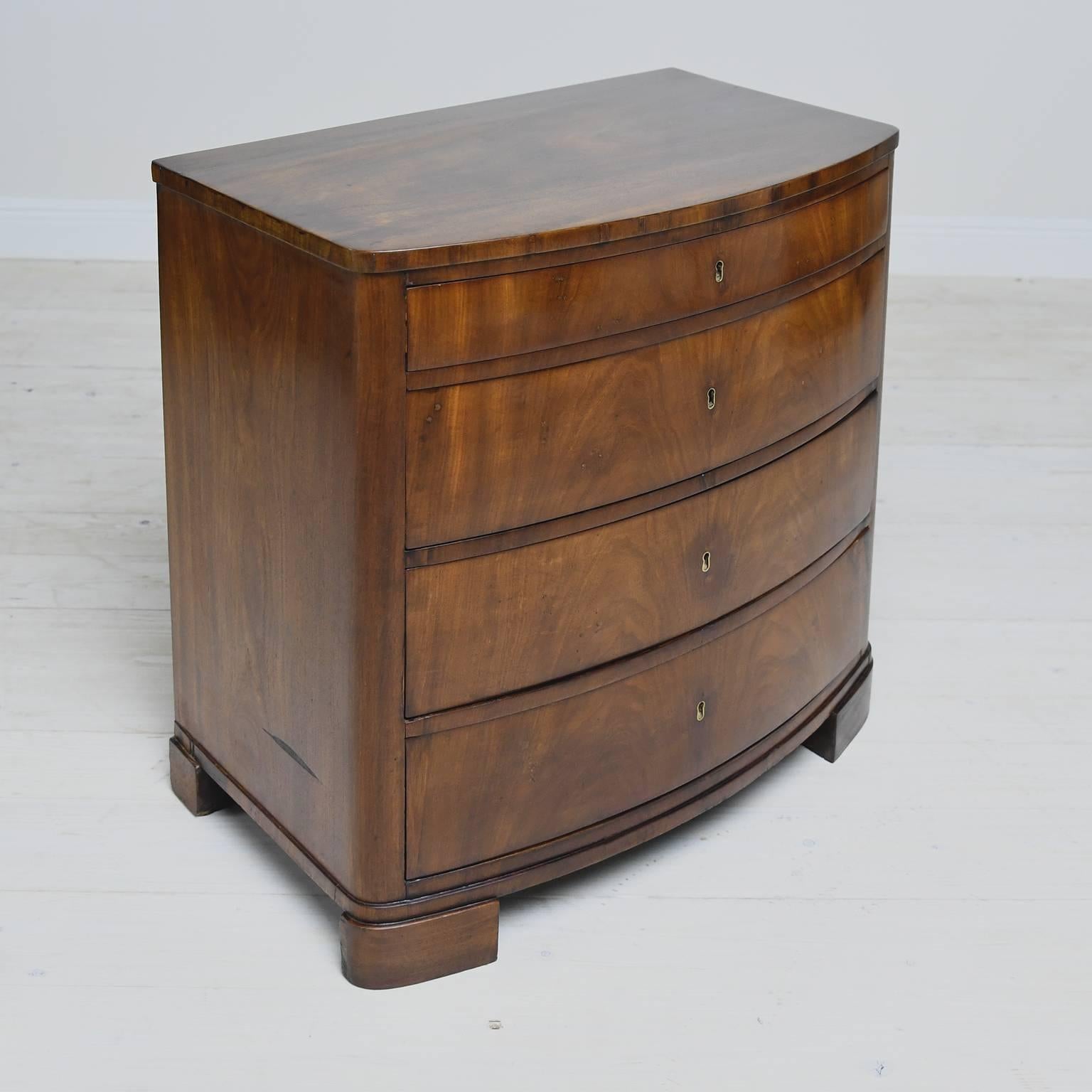 A small Biedermeier chest from during the Danish late empire period with bowed drawer fronts in bookmatched crotch mahogany offering four drawers, circa 1830. This form is unique to Denmark in terms of scale, proportions and simplicity of design. It