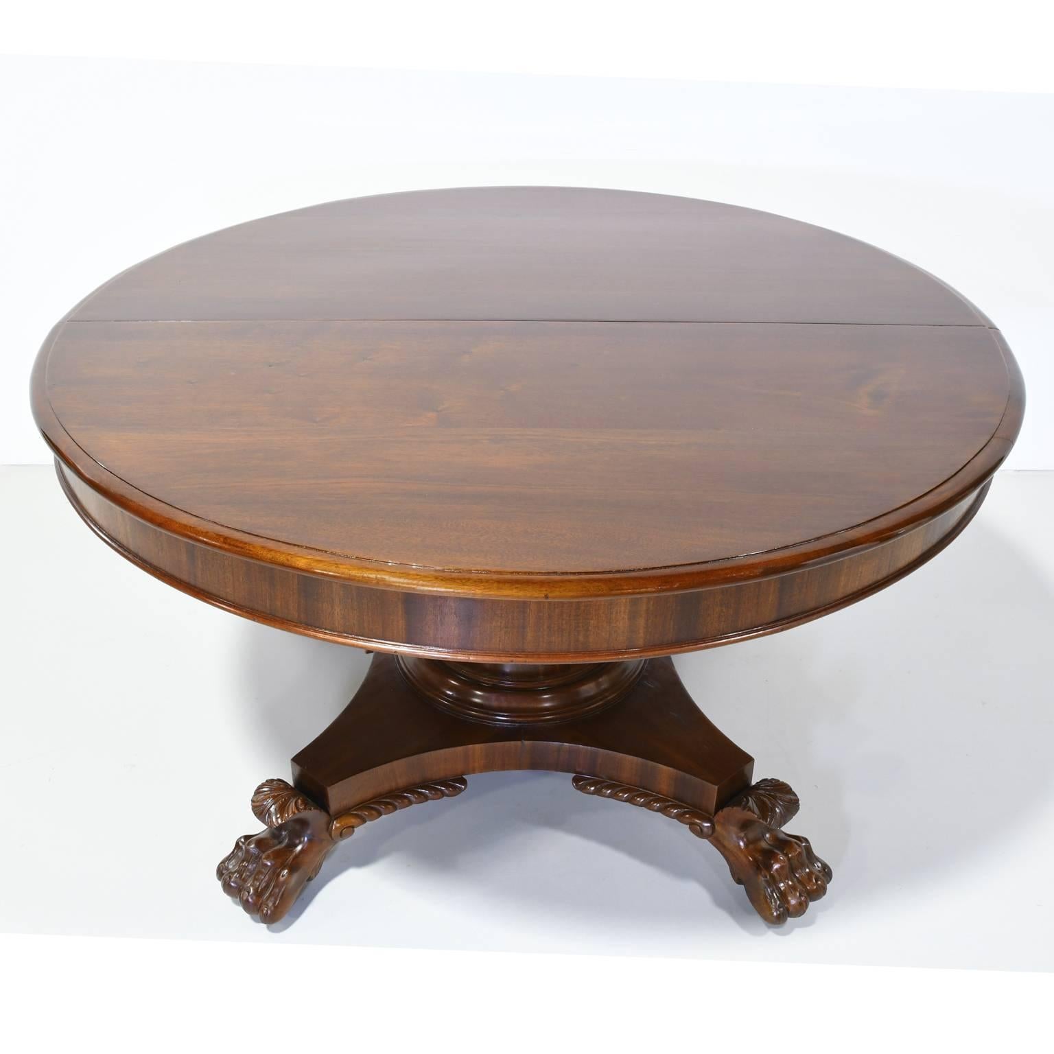 A classical American Empire extension dining table in mahogany with round top and apron over cylinder pedestal resting on quatre-form base ending with carved lions' paw feet. Includes four original leaves/plates, New York, circa 1830, seats 10
In