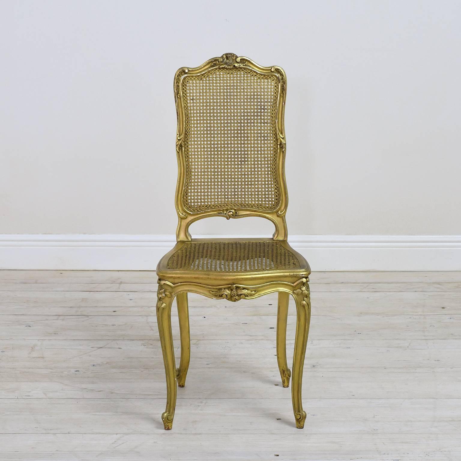 A fine pair of chairs in gilded wood in the Louis XV style with all of the hallmark ornamentation: Rocaille carvings on crest, seat apron and knees, with legs on cabriole. Hand-caning on seat and back. France, circa late 1800's.

Measures: 26"