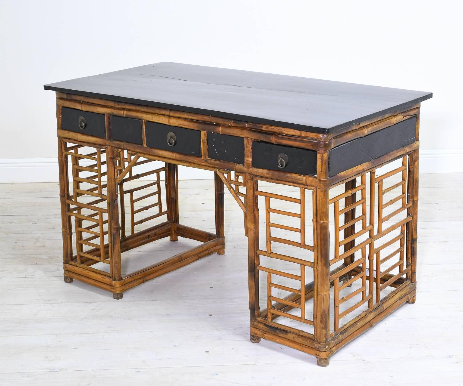 A charming writing desk in bamboo with open lattice work on pedestals, ebonized top and apron, and offering three storage drawers embellished with floral work over ebonized finish, China, circa 1930.

Desk may float since it has finished