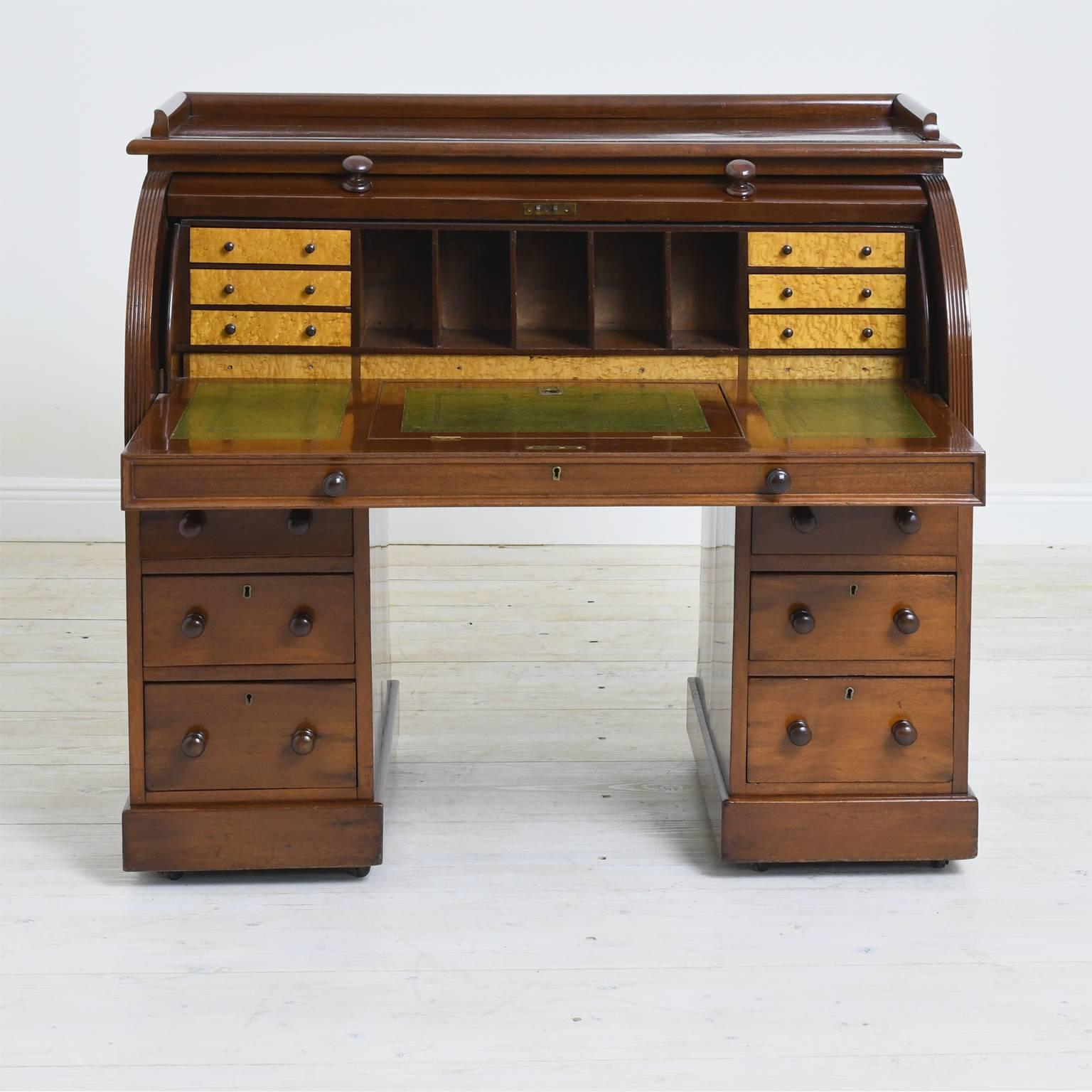 A beautiful and practical working desk in mahogany on two pedestal bases offering six storage drawers and with pull-out desk drawer and cylinder top opening to a series of small interior drawers and open cubbies for letters and bills. Features