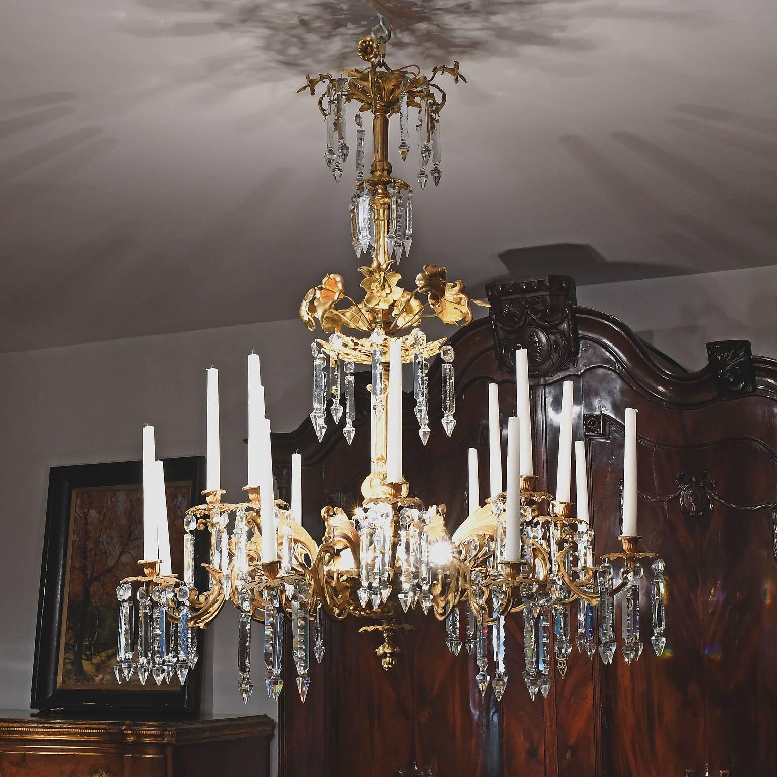 An elegant French Rococo-Style chandelier in gilt bronze with beautiful glass crystal prisms, that holds 16 candles but has also been electrified to accommodate six 25-watt candelabra bulbs. Bulbs are located on top of the bottom dish where the arms