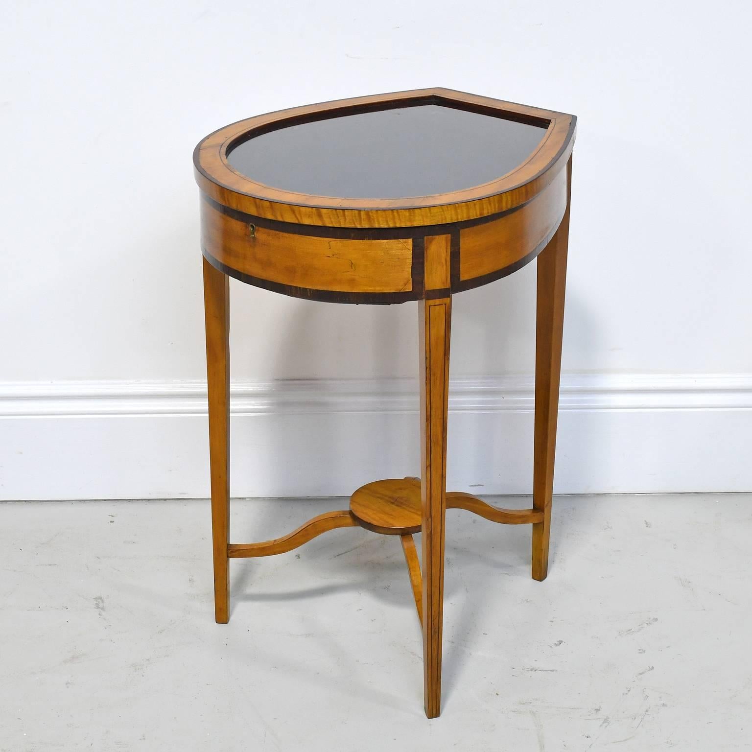 A pair of Edwardian satinwood vitrine tables with shaped tops with banded edges above single drawer, and raised on square tapering legs with string inlay, joined by stretchers surmounted by circular shelf. Tables have glass tops with deep wells to