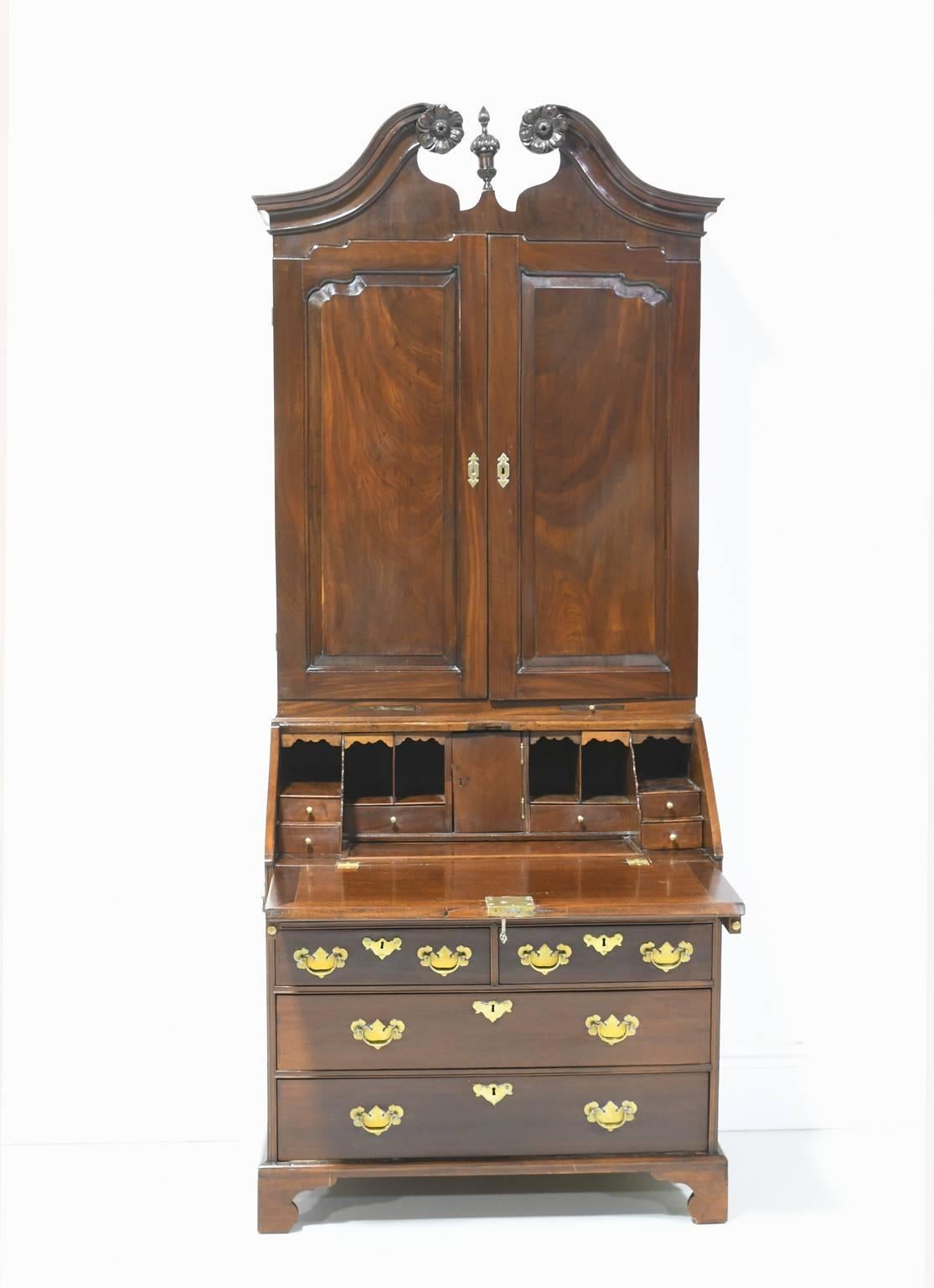 A fine 18th century George III English bureau bookcase secretary in solid West Indies/ Cuban mahogany. The bonnet features a swan neck, broken-scroll pediment with carved rosettes and a center finial. Upper solid door panels are raised and interior