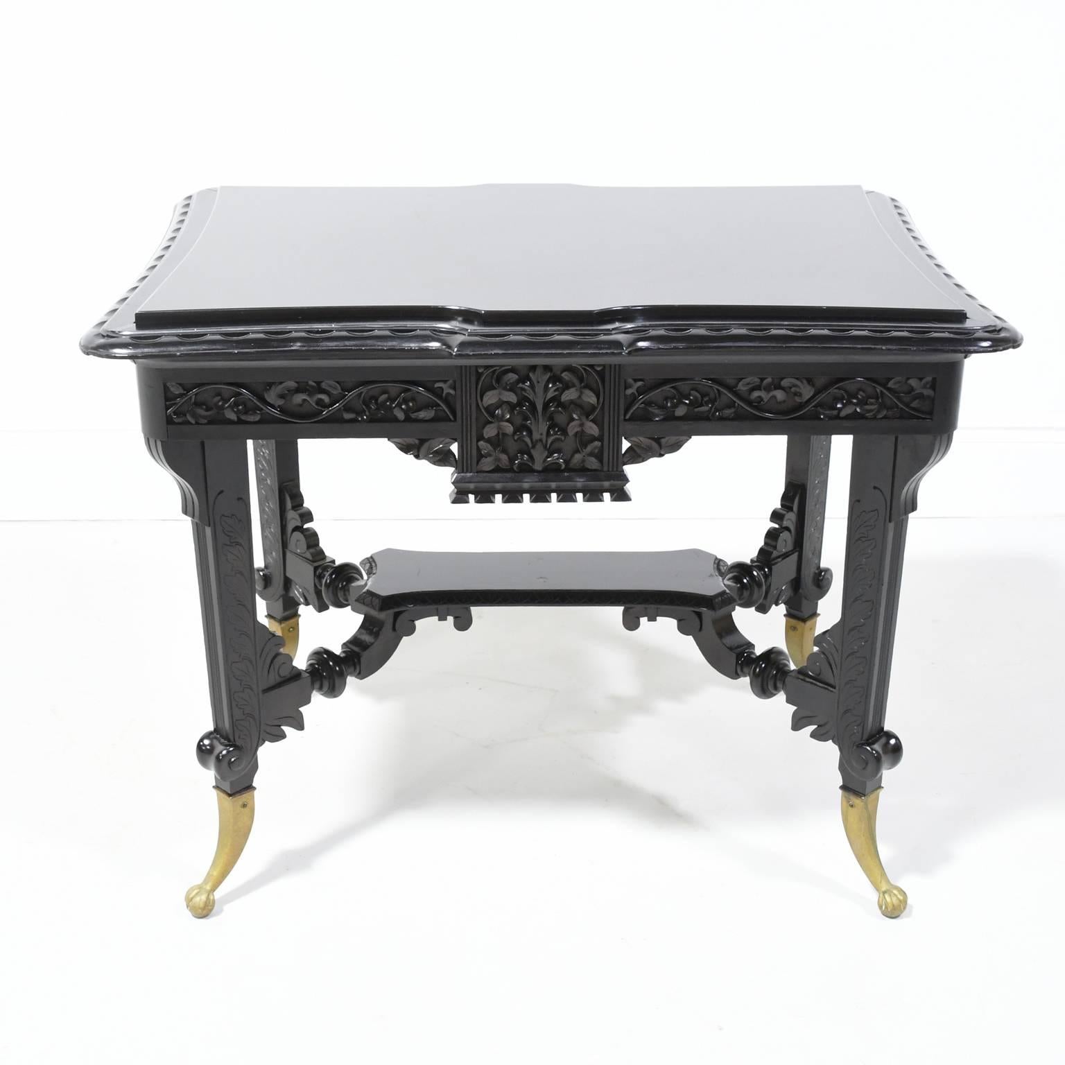 An exquisite table from the Aesthetic Movement of the late 1800s, in ebonized wood with a Belgian black inset marble-top, carved foliage along the apron, carved stretcher supporting bottom shelf, and carved legs resting on brass feet. American (or