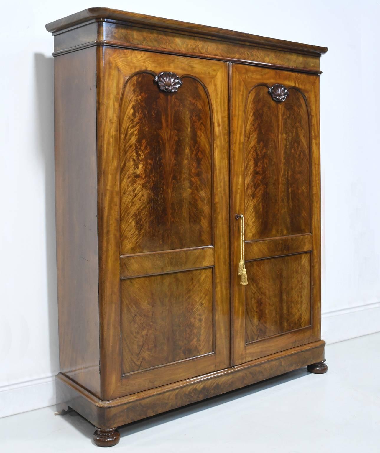 A striking French Louis Philippe armoire with two doors with large figured mahogany panels and carved shell motif. Interior has original adjustable shelving and drawers. Makes an ample closet with room for hanging, drawer space and offering lots of