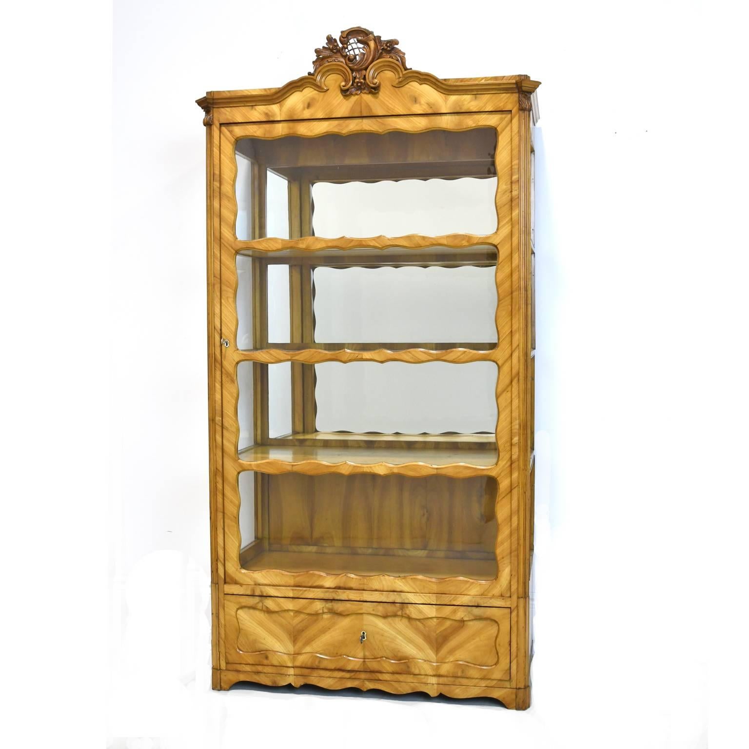 A very lovely display cabinet or vitrine in cherrywood with original glass door, glass side panels and mirrored back, with carved bonnet. Offers one storage drawer with working lock and key. Germany, circa 1850.

Measures: 38 1/2