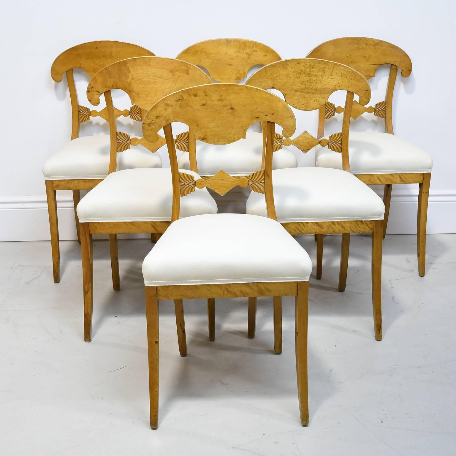 A set of six early Swedish Biedermeier dining chairs from the Karl Johan era with carved crest rail in the shape of a soldier's hat, and a carved diamond flanked by stylized foliage on the lower back rail, tapered front legs and saber back legs, and