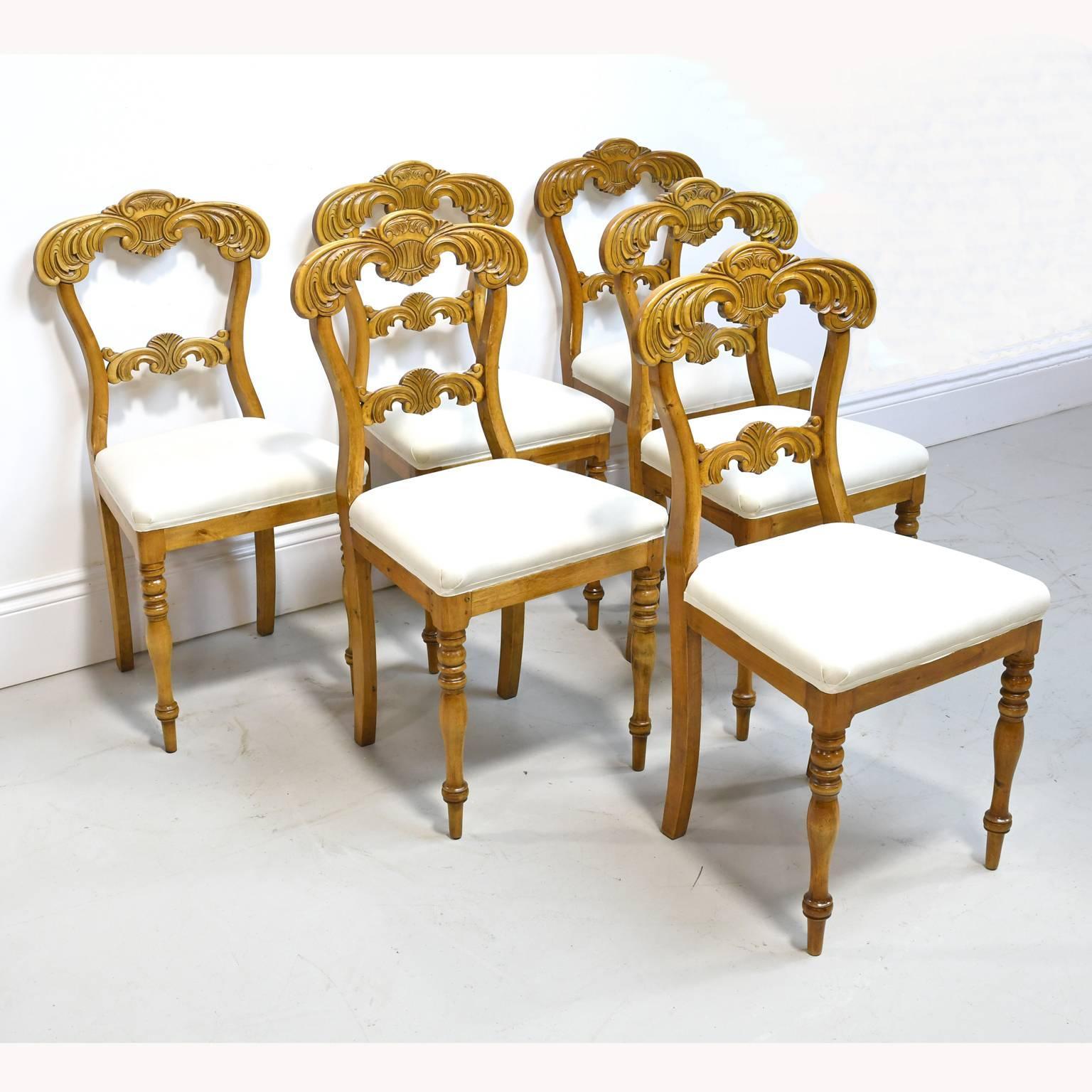 From the reign of the French-born Swedish king, Karl Johan, a very lovely set of six dining chairs in birch with foliate carvings on crest and bottom back rail, with turned front legs and saber back legs and upholstered seat, Sweden, circa