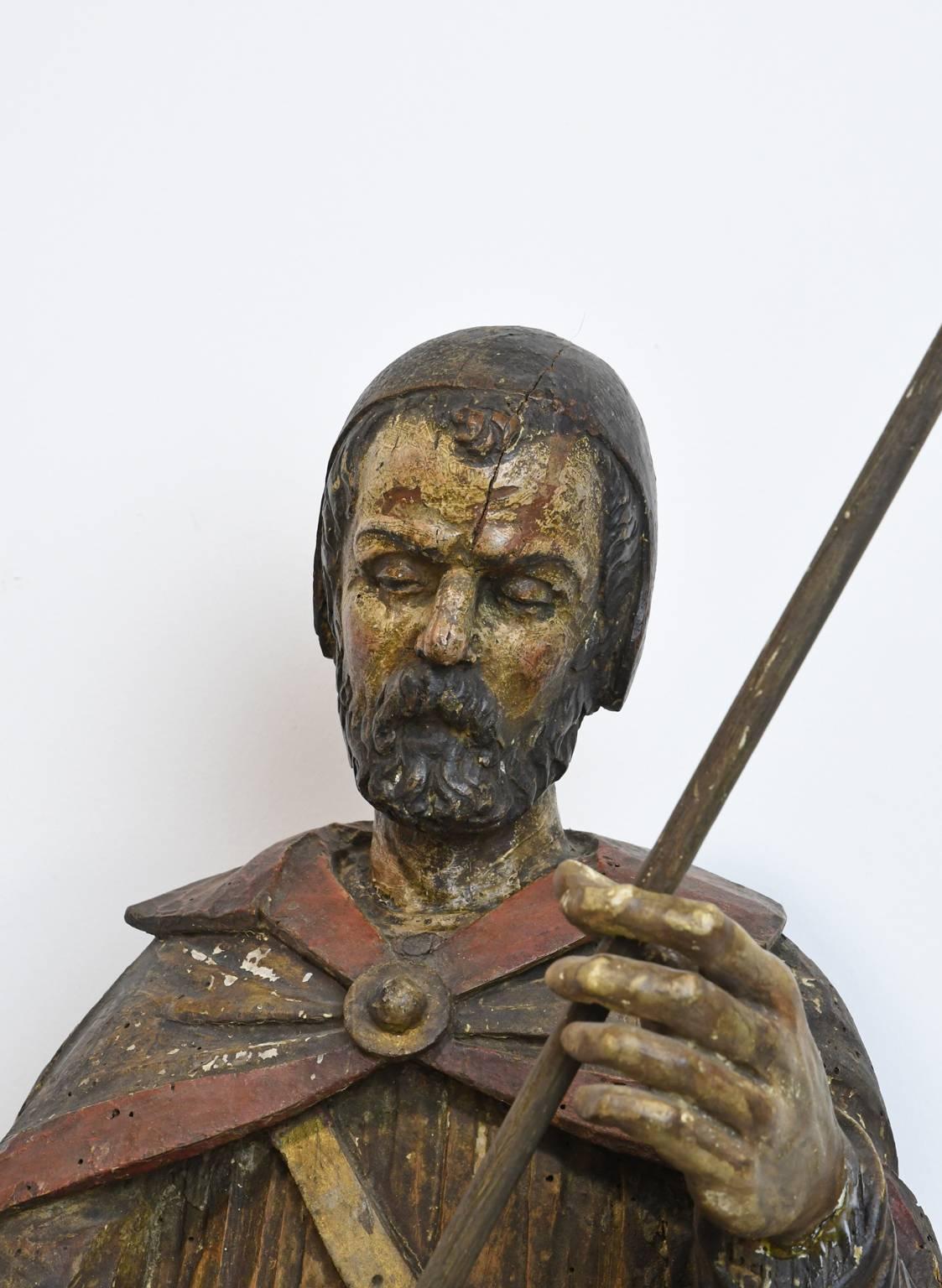 A captivating depiction of Saint Roch (or San Roque) in carved and polychromed wood holding a staff and dressed in pilgrim's clothing, with a dog on one side and an angel on the other. The angel exposes a wound in his upper thigh, a reference to the