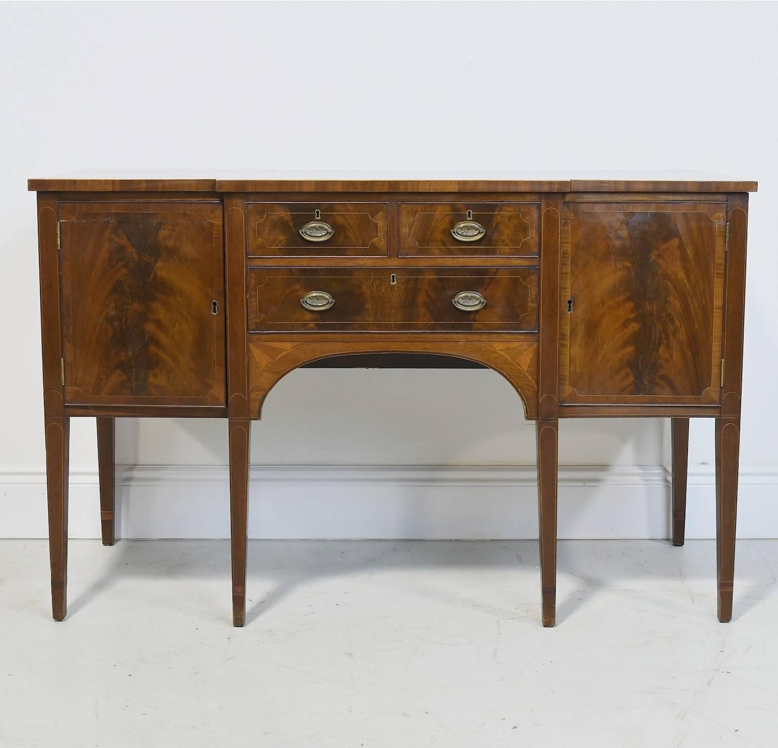 A late 19th century Hepplewhite-style sideboard in mahogany with line inlays on the drawer fronts and on the legs. Doors are edge-banded & have figured mahogany veneers on door panels and drawer fronts. Hardware is original to cabinet. Sideboard was