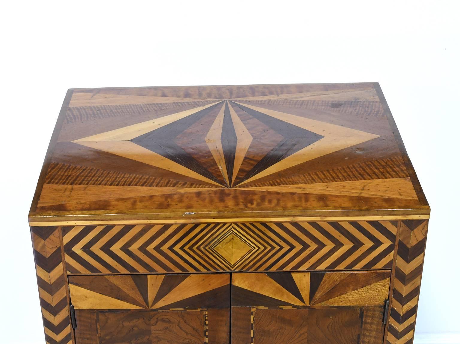 A very lovely Art Deco cabinet in mahogany and walnut with inlays in tigerwood and satinwood in a geometric pattern, offering two doors. American, circa 1920. 

Measures: 20 1/4