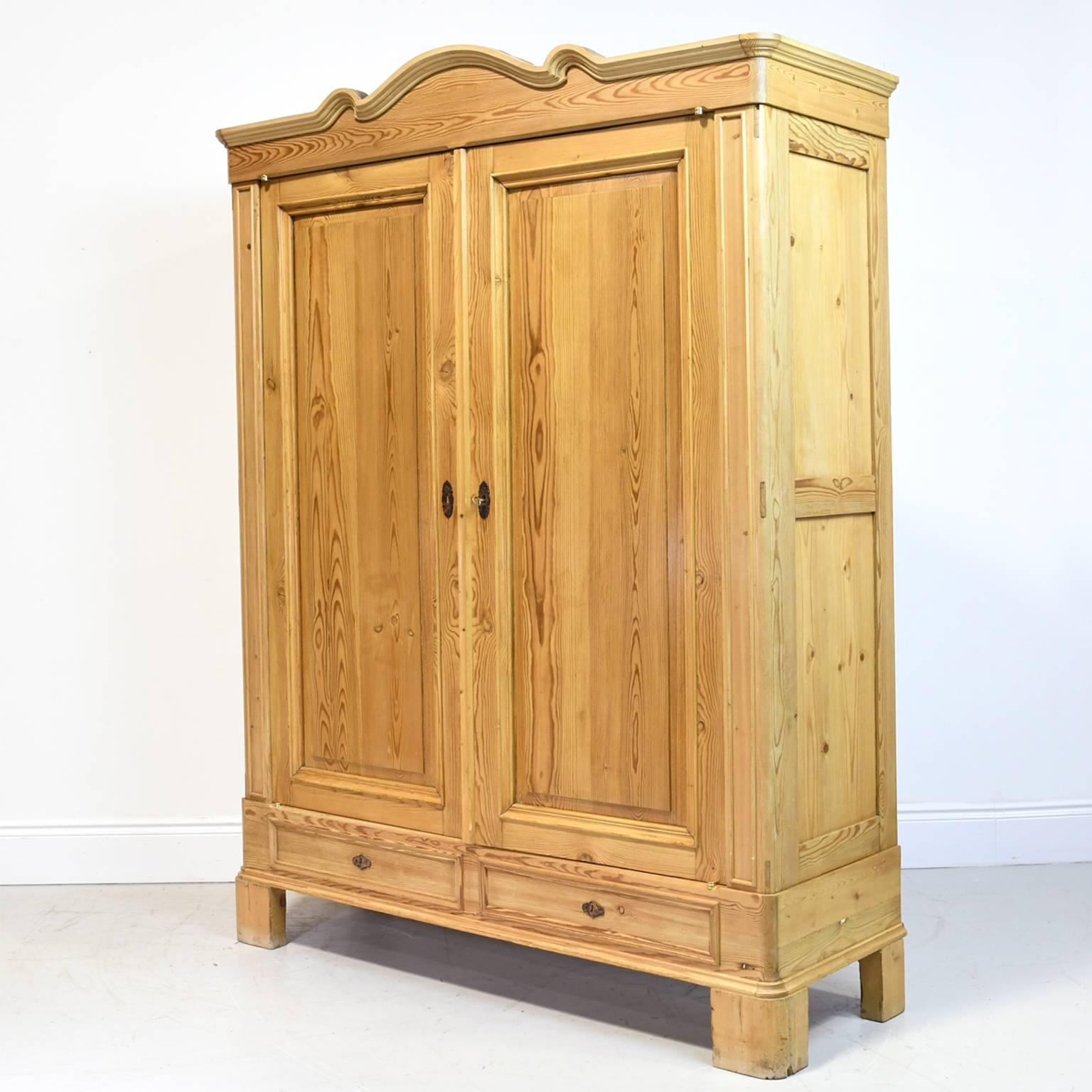 A large and handsome North German pine armoire with original curved bonnet, two paneled doors, two exterior drawers with original leather escutcheon key plates, and interior shelving, circa 1825. 
Offers lots of storage for clothes or linens!