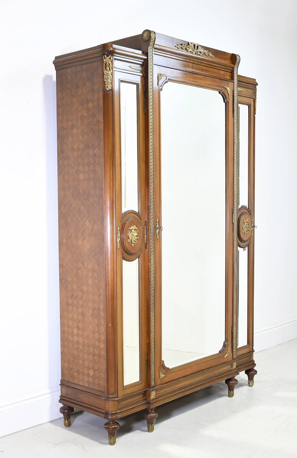 A very fine Napoleon III French armoire in the style of Louis XVI in walnut with bronze dore/ gilt ormolu mounts that include ribbons, sheet music and various musical instruments. Other details include parquetry sides, a stepped bonnet, three