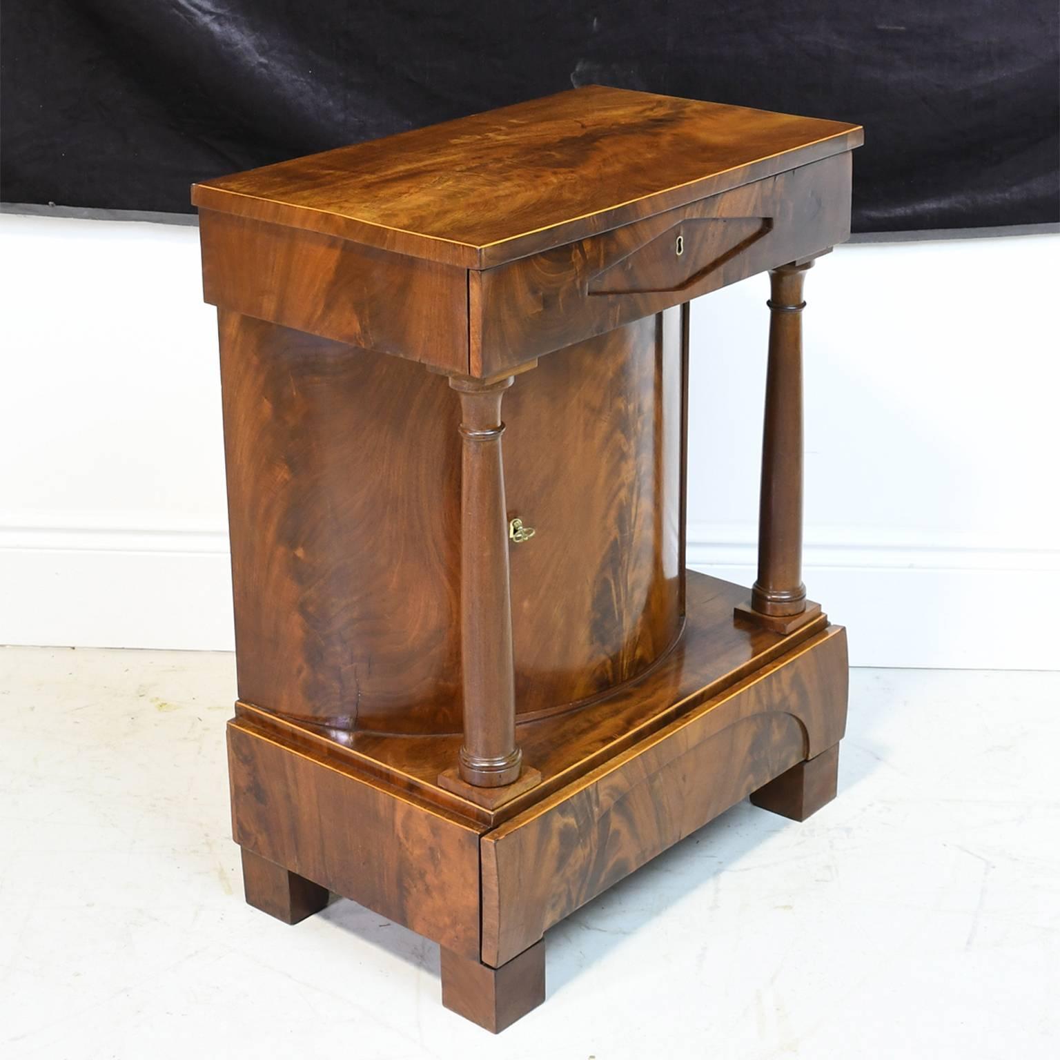 A very handsome and architecturally strong Biedermeier /Empire console or small cabinet in mahogany with small satinwood inlaid line work, with full turned columns flanking a central bowed front cabinet, with one drawer above and another below, and